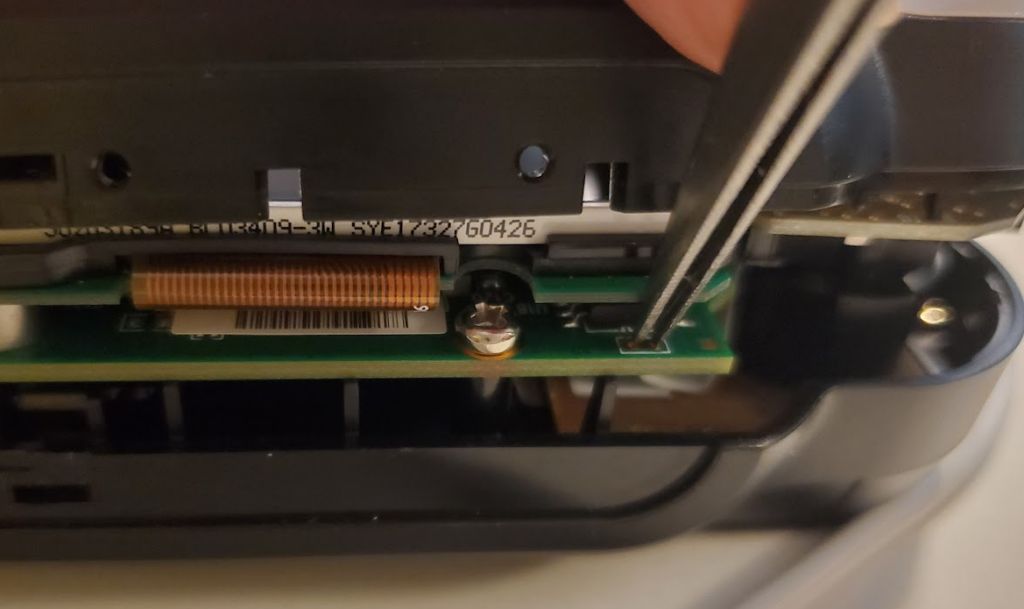 Picture of tweezers being used to short a pcb connector through the side of a case that's been slightly cracked open.