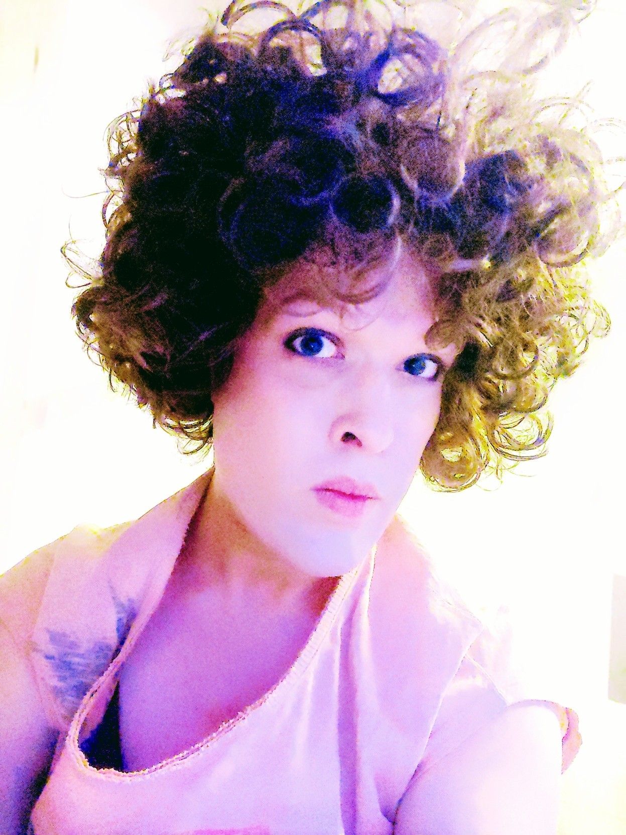 Colourfully filtered picture of me looking down at you with an expression like I'm examining you, my hair floofed up in circular curls