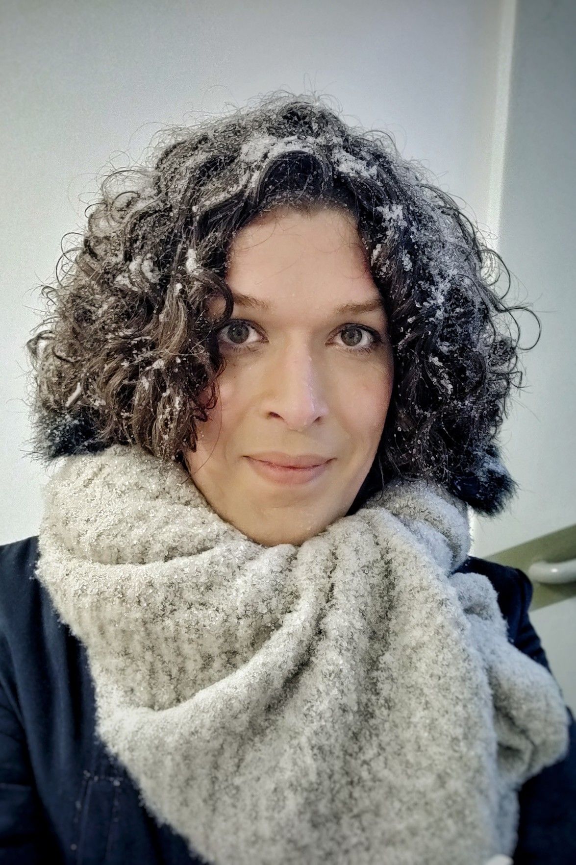 Selfie in a big grey scarf, taken indoors but there's snow in my hair as I was just outside.