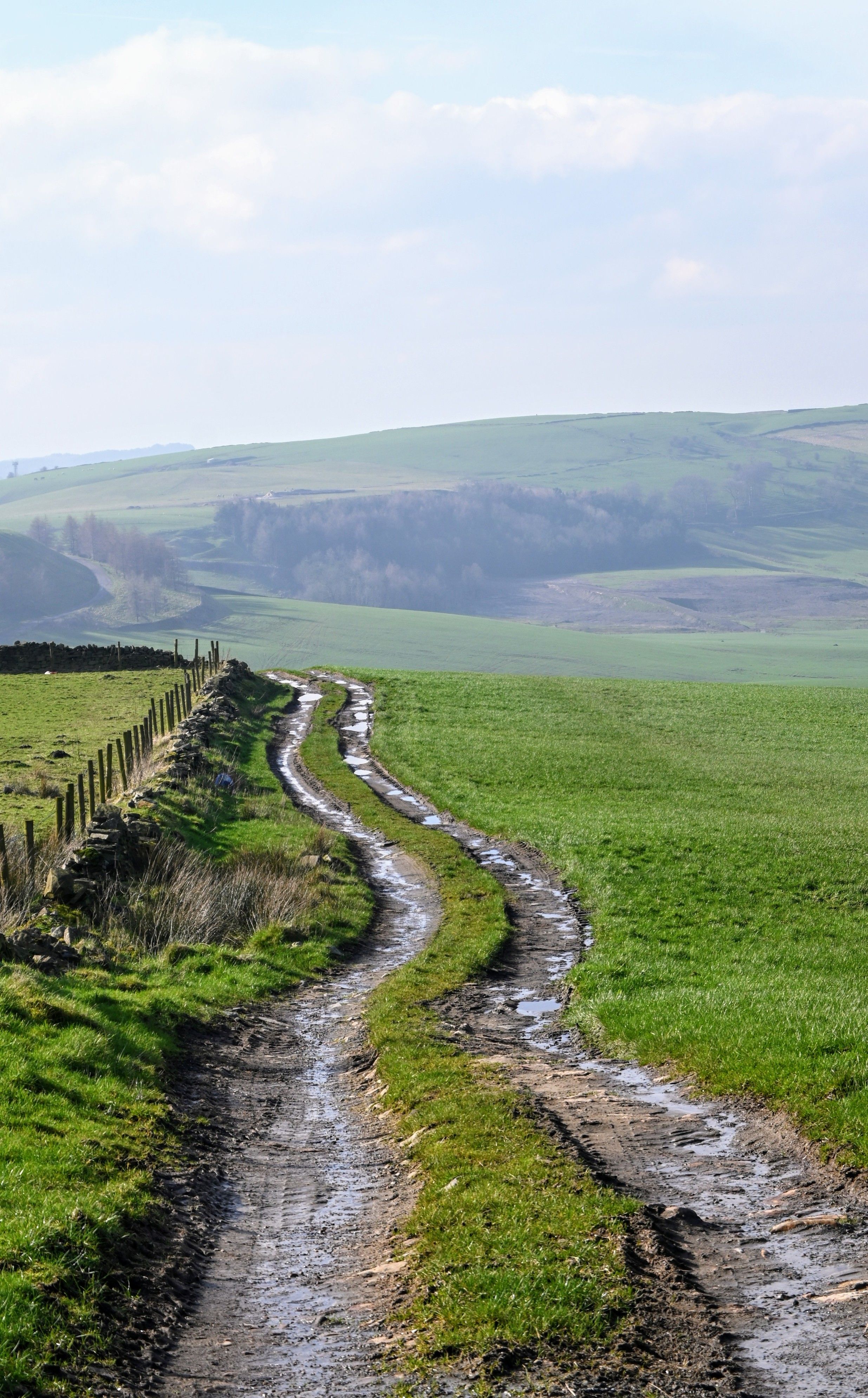 Muddy winding track across a field with hills in the distance 