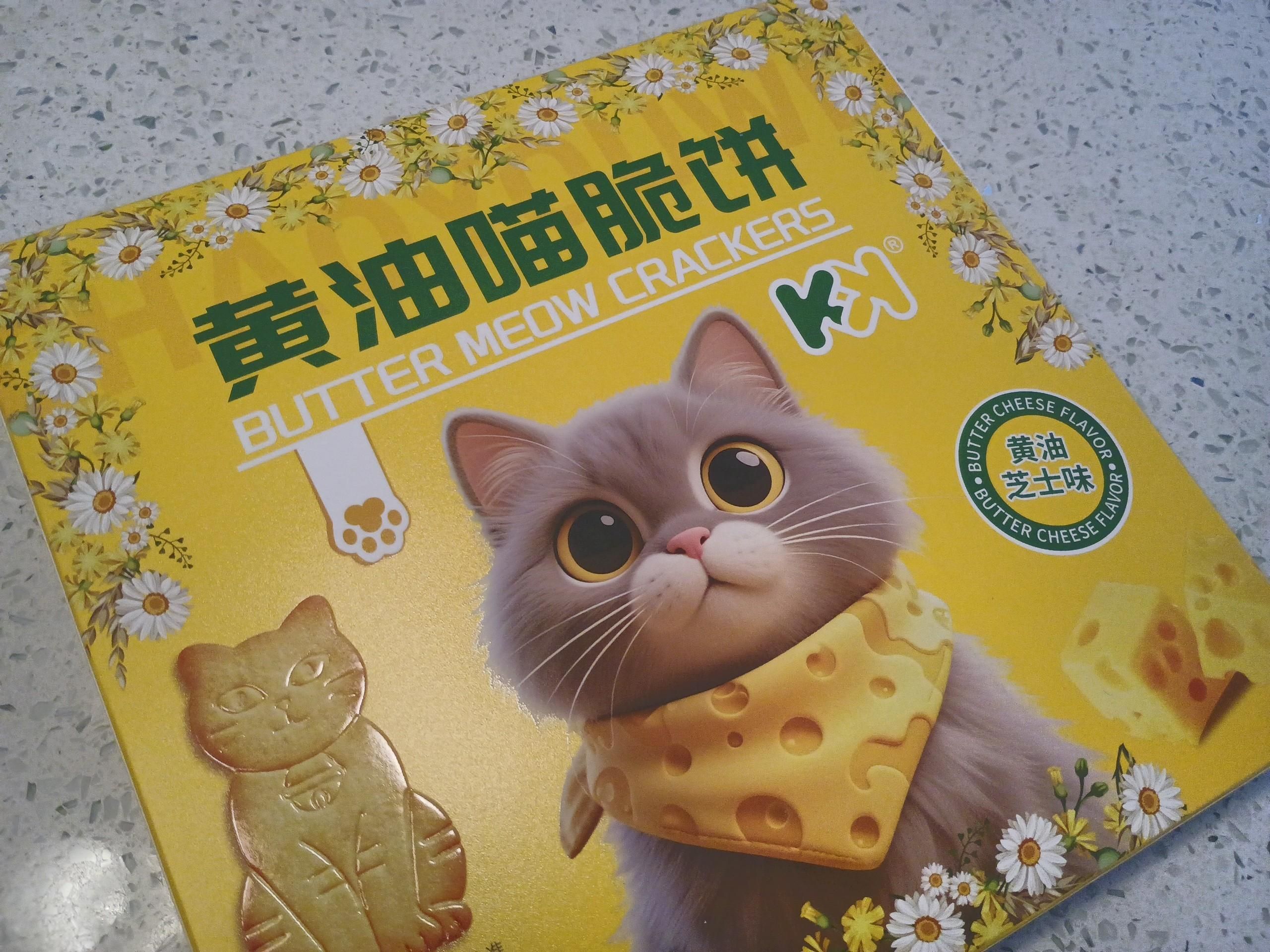 A square box about the size of a large book, which is yellow with Chinese characters on it and features a cute big-eyed cat graphic, wearing a napkin around his neck which looks like Swiss cheese.