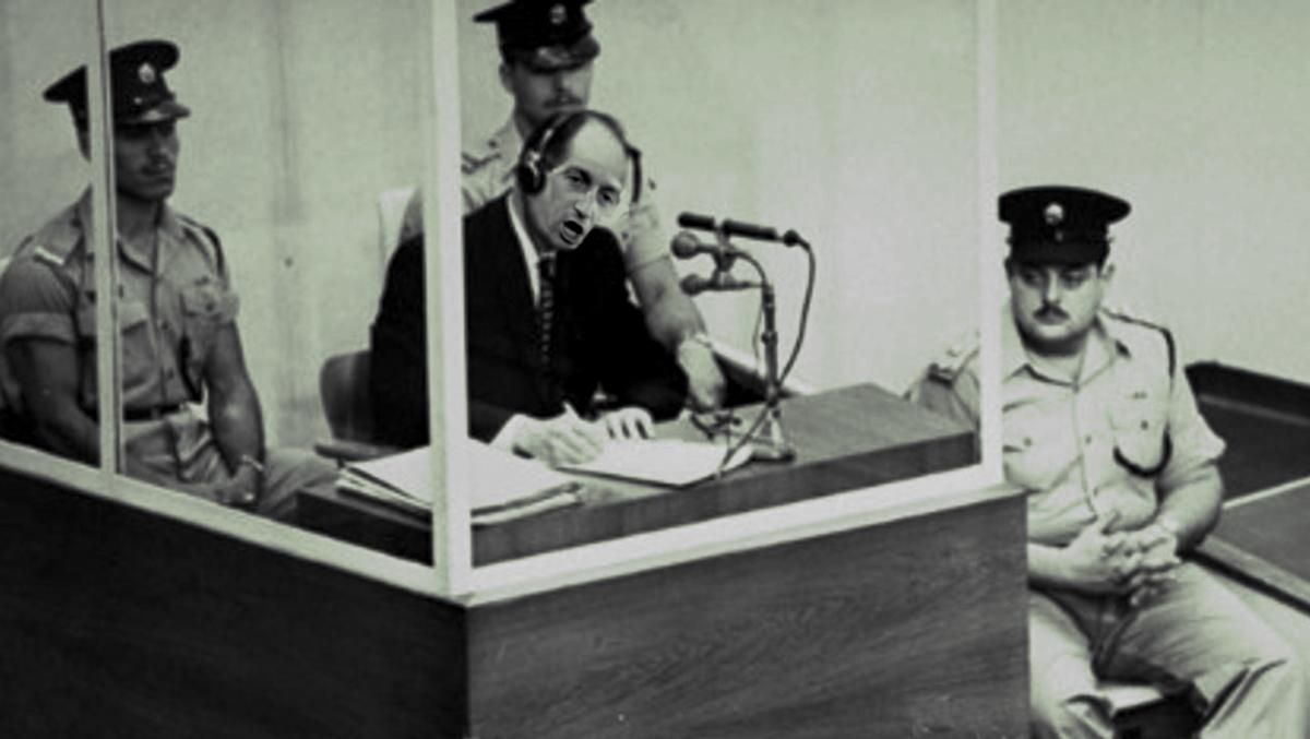 A famous 1961 photo of Adolf Eichmann on trial in Jerusalem; Eichmann's face has been replaced with the face of Stephen Miller.

Image:
Gage Skidmore
https://commons.wikimedia.org/wiki/File:2025_-_Stephen_Miller_(cropped).jpg

CC BY-SA 3.0
https://creativecommons.org/licenses/by-sa/3.0/deed.en