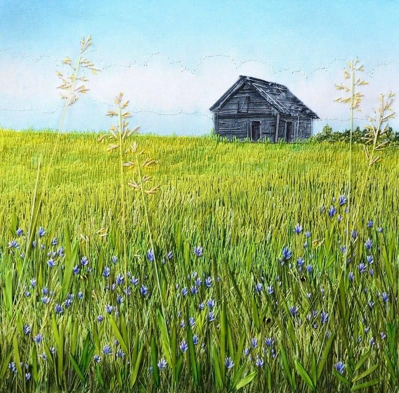 Pictorial textile artwork featuring a grey barn in a field with long lush green grass with small blue flowers under a pale blue sky
