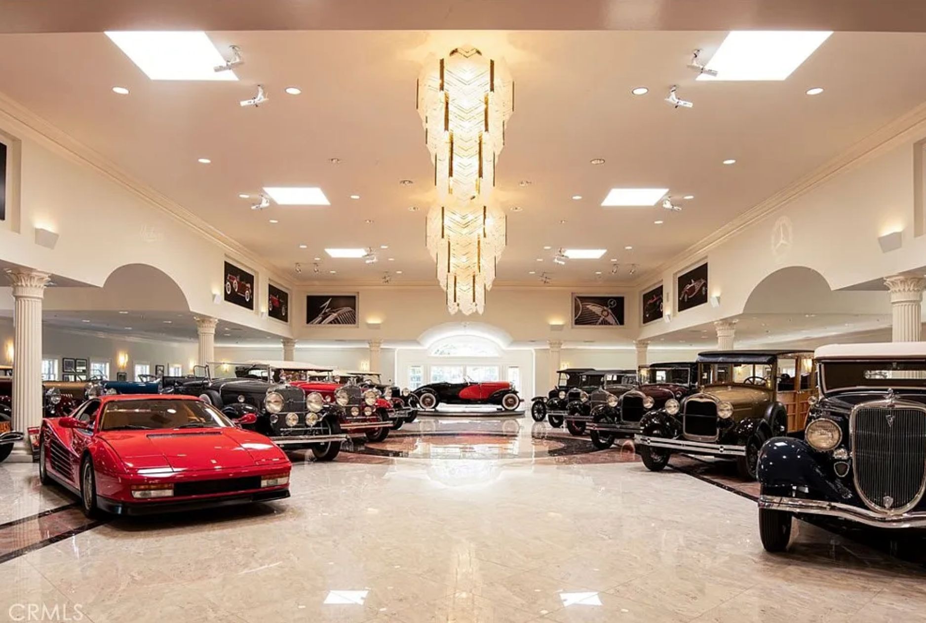 A large room that according to the listing can contain up to 70 cars. It has a marble floor and large chandeliers. In the room are a variety of vintage cars, all of which would be extremely expensive. 
