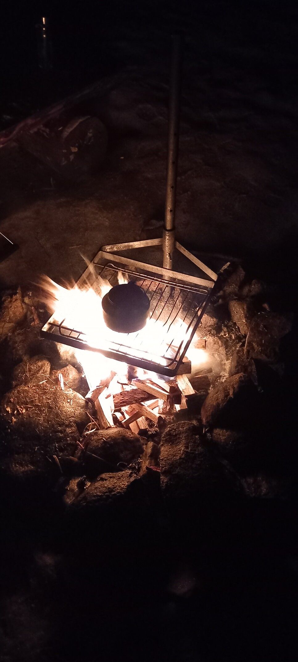 A coffee pot on a grill above camp fire. Darkness all around the fire. February evening in Finland.