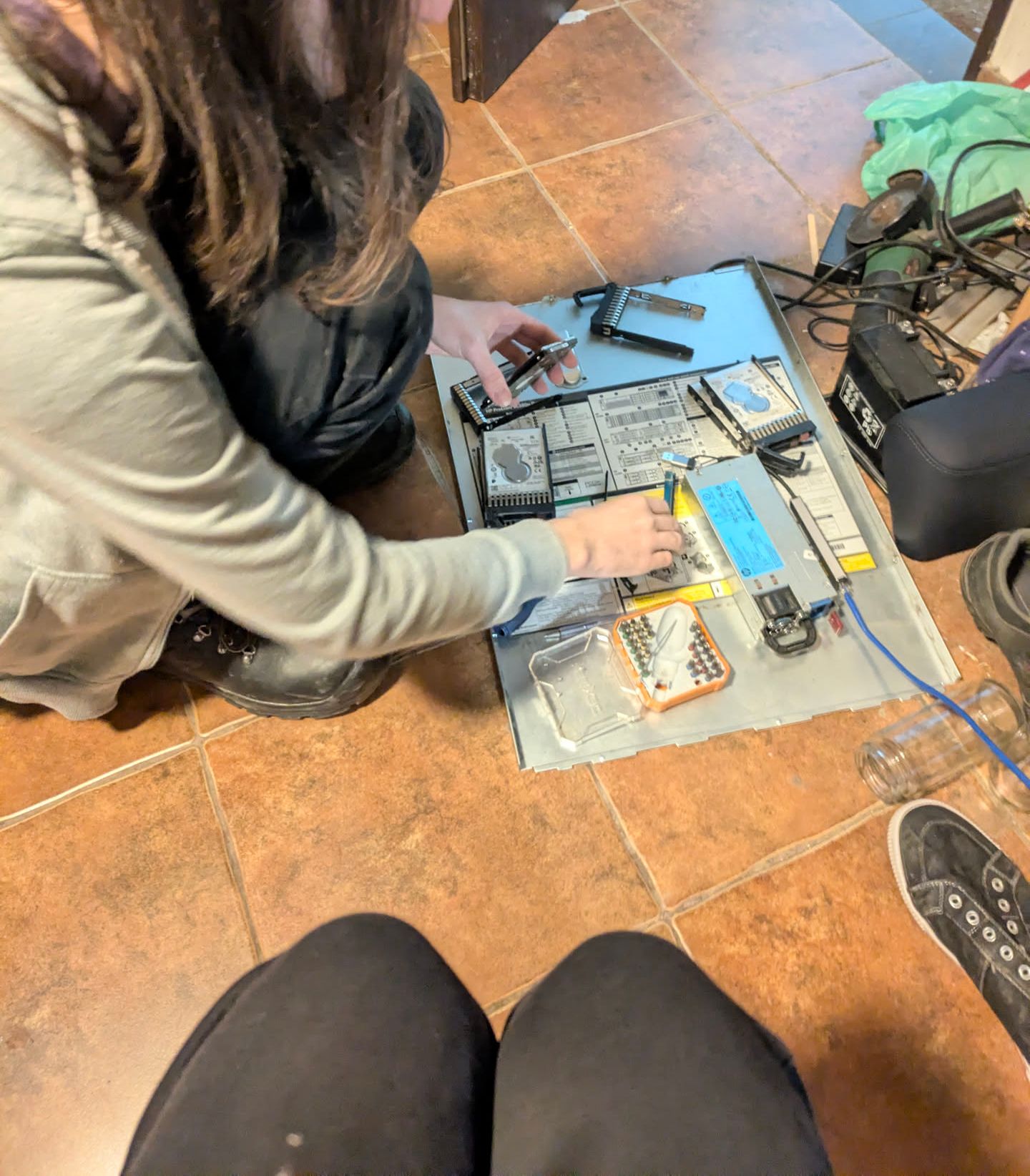 aria fixing a 2.5 disk in a newer HP caddy, with the top server cover plate on the floor, filled with disks, loose caddies and screwdriver bits