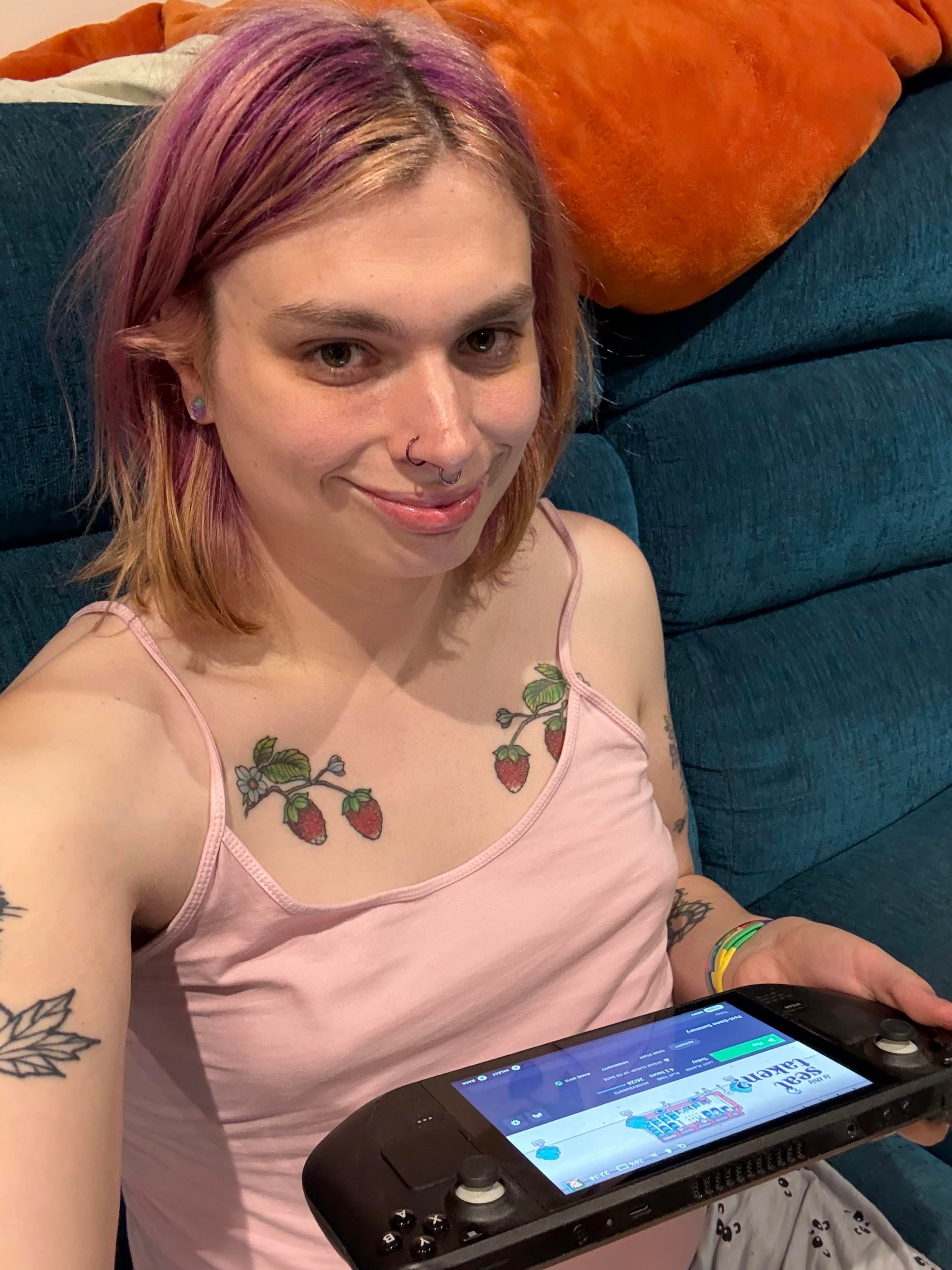 A selfie of Liv sitting on the sofa holding a steam deck with the page for the game visible on the screen. She’s wearing a pink camisole top.
