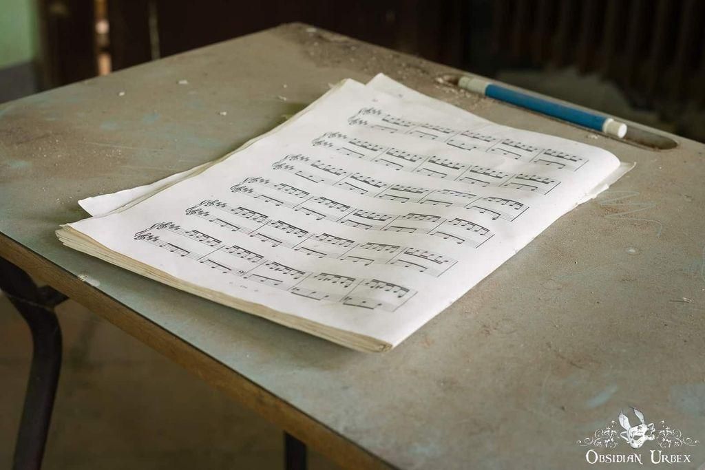 Dusty music sheets rest on an aged desk, accompanied by a blue pen. The image,