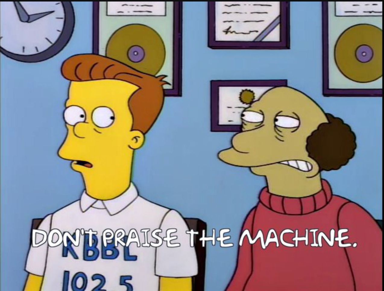 A screenshot from the Simpsons of two radio DJs. One says to the other “Don’t praise the machine.”