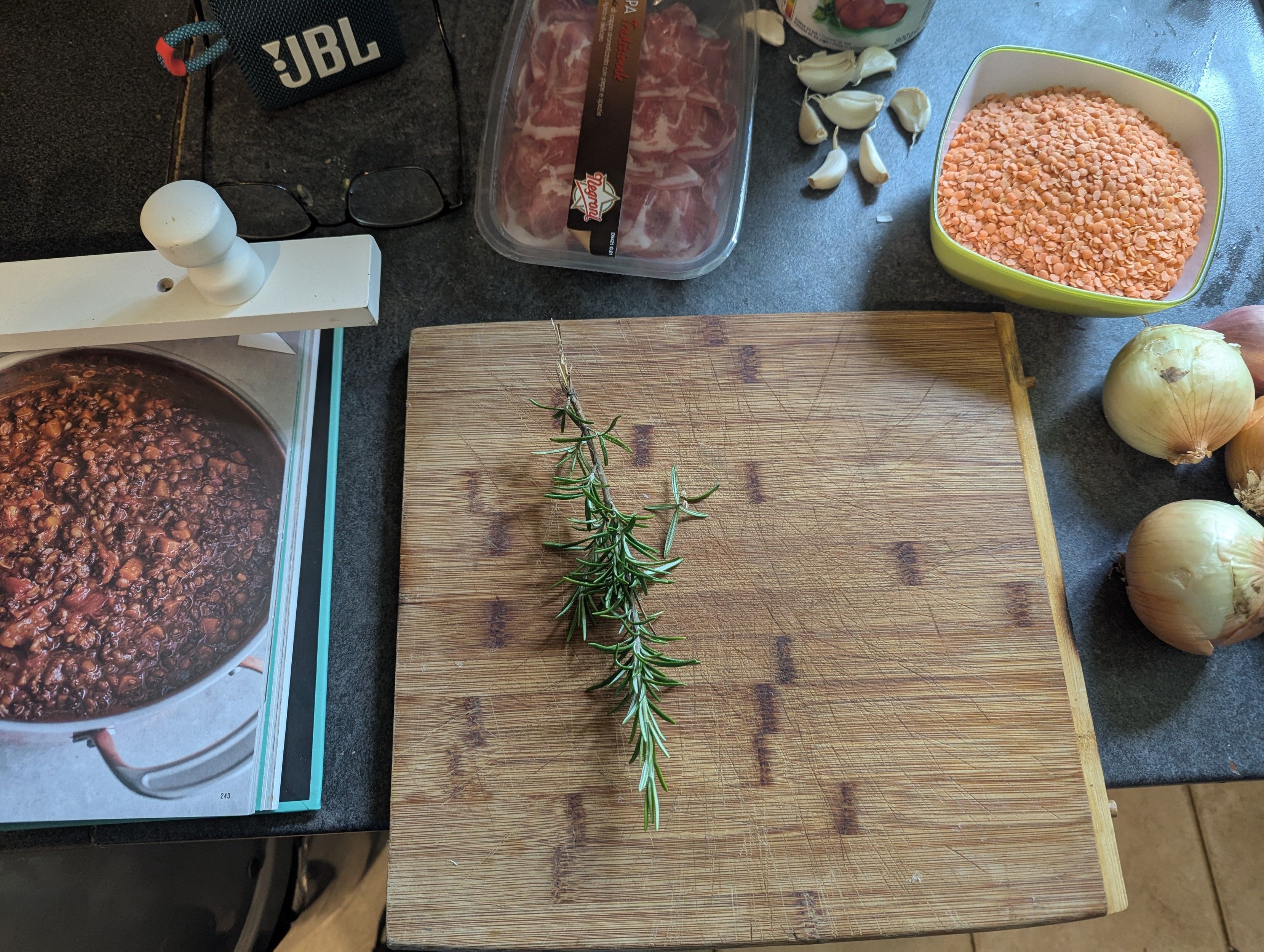 Various ingredients including rosemary in the chopping board, onions, garlic, lentils, cured ham, plum tomatoes. Minced steak still in the fridge.
