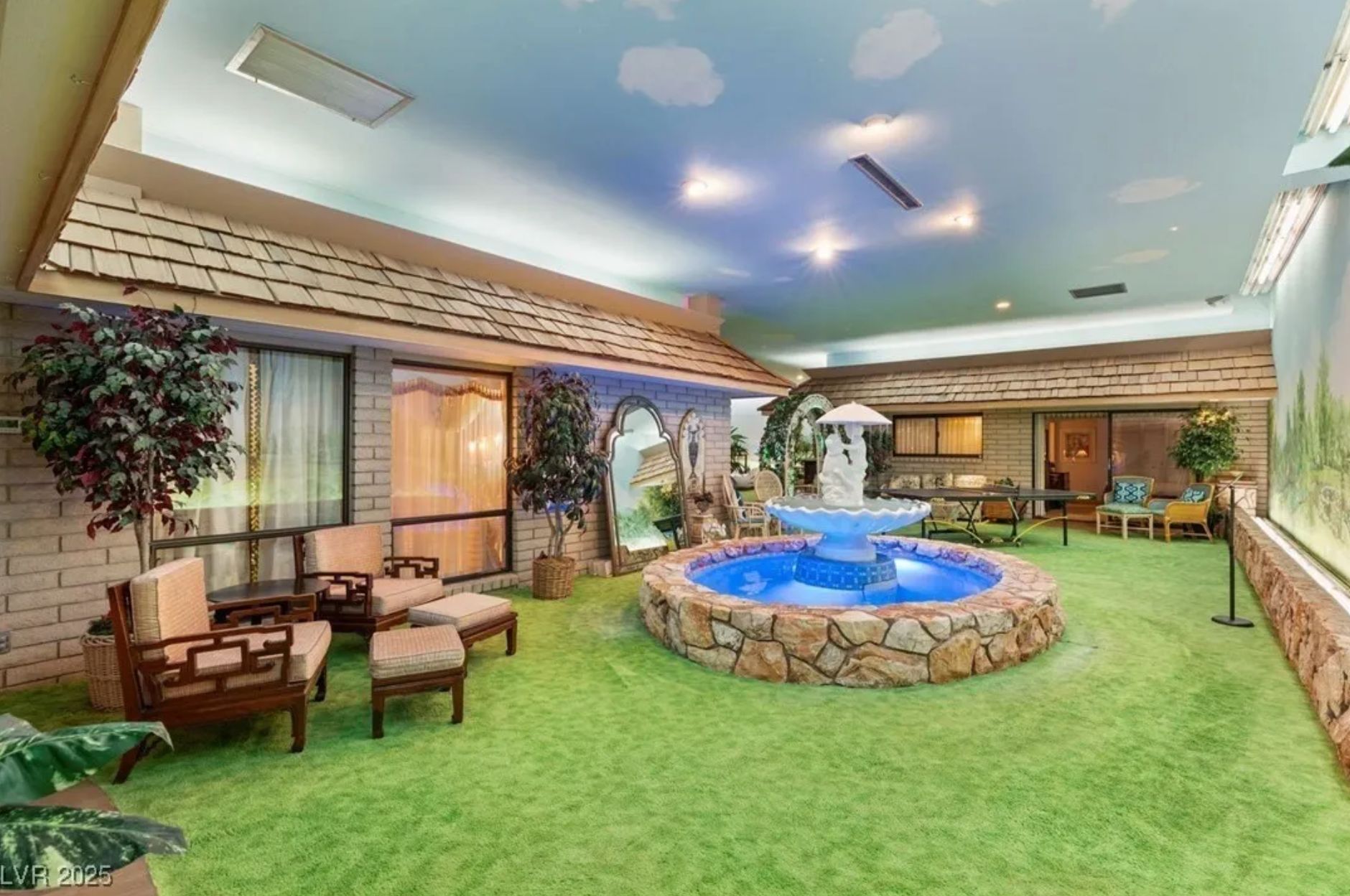 Another view of the underground house showing a courtyard with fake grass and a fountain, and the ceiling is painted with clouds. 