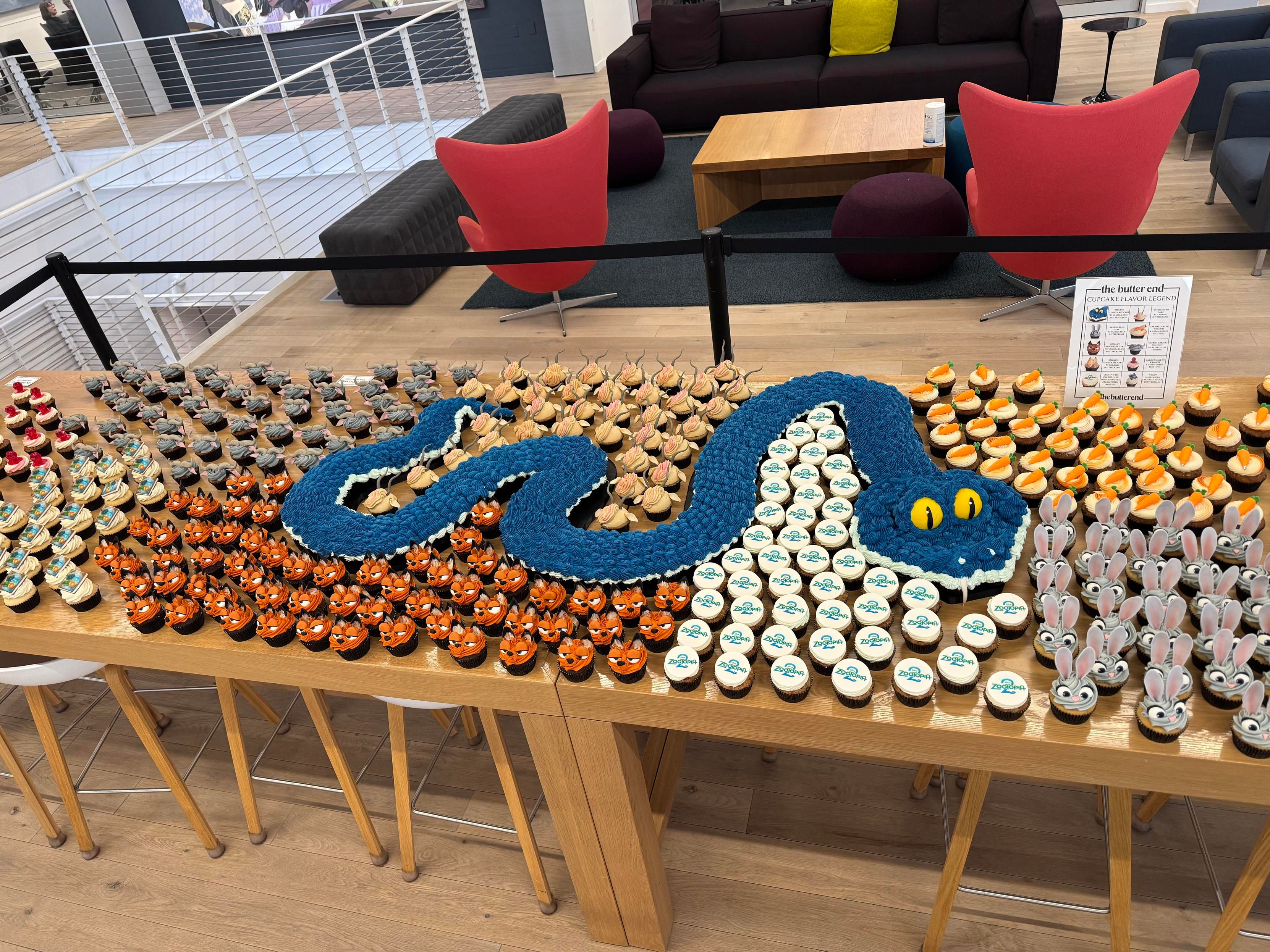 Table covered in Zootopia-themed cupcakes, with a Gary the snake cake twirling in the middle of it all.
