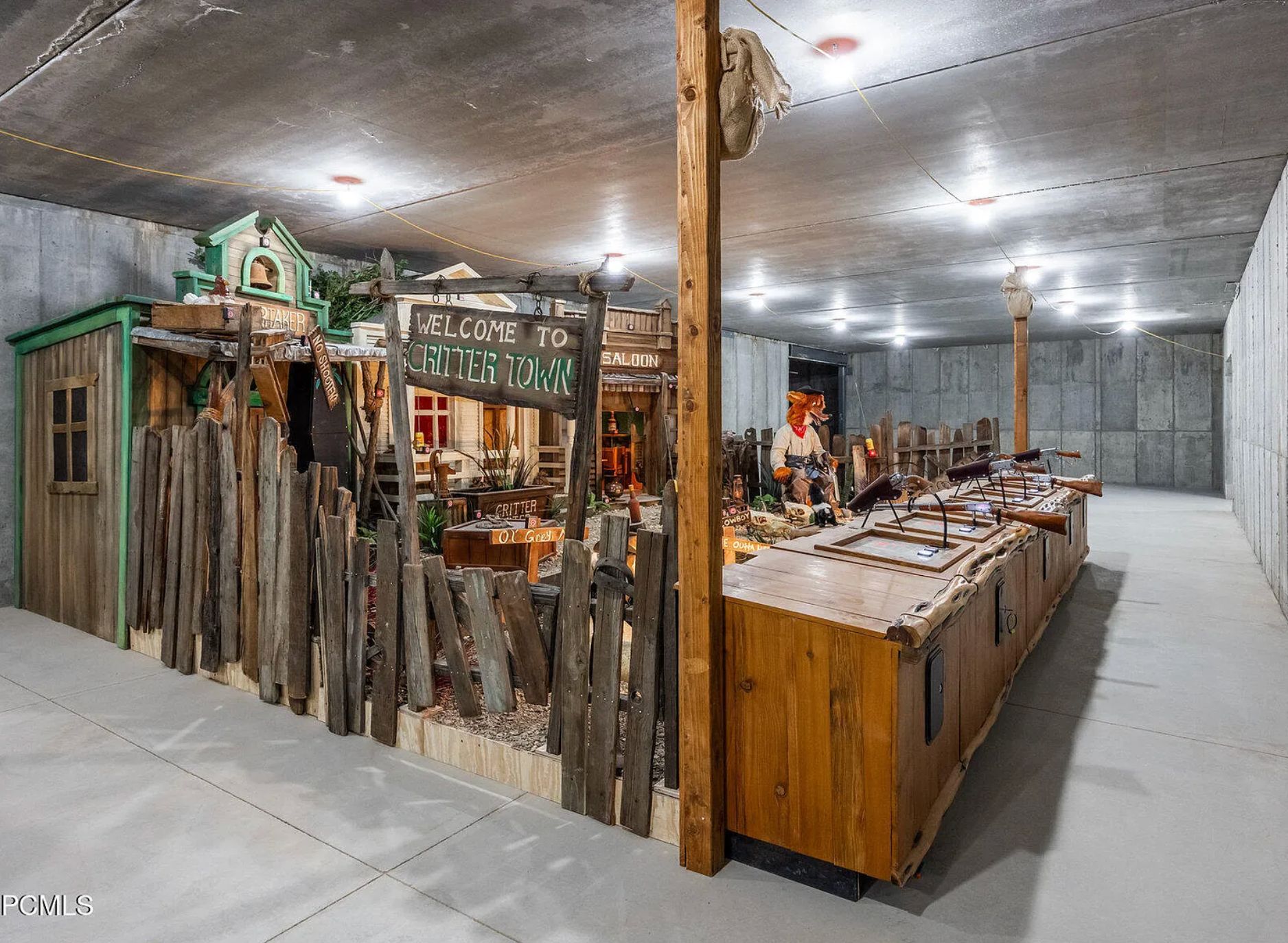A concrete basement with a sign saying "welcome to crittertown" and it's a sectioned off area with a rickety wooden fence and a block with fake shotguns across it for play shooting, and a very creepy large stuffed fox. 