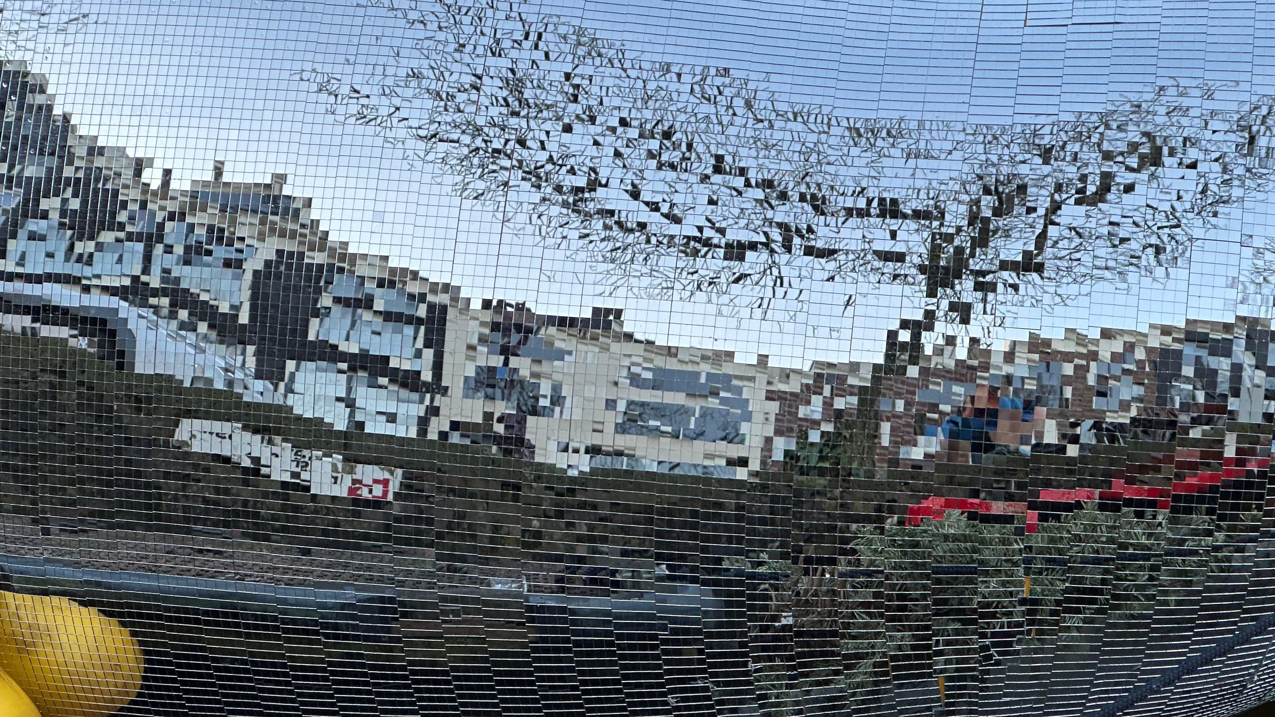 boat covered in disco mirrors reflecting the canal houses and a tree as tiny squares of color