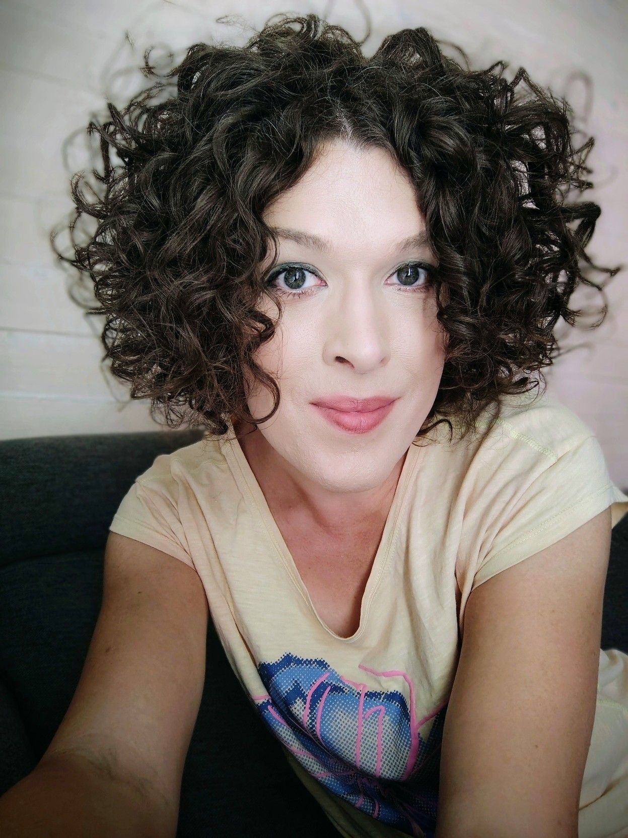 me smiling, sitting on the sofa leaning forward towards you. curly brown hair with lots of volume, a yellow top with a big blue and pink flower print