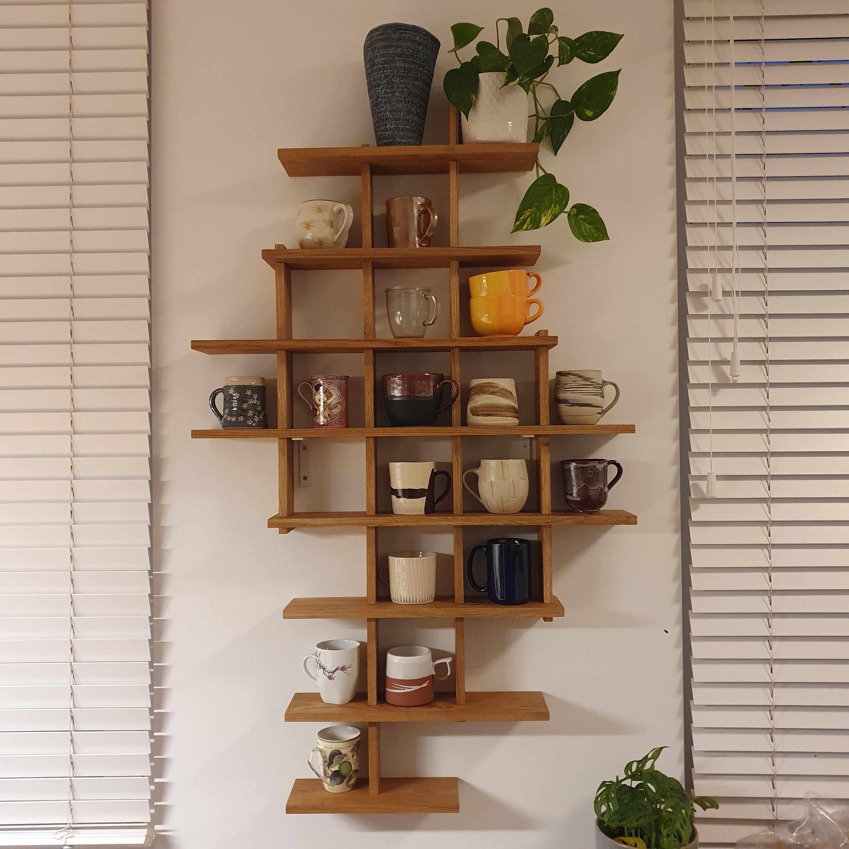 An asymmetric shelf with individual rectangular spaces for well over 20 mugs, filled with a collection of different mugs, most of them handmade ceramic. 