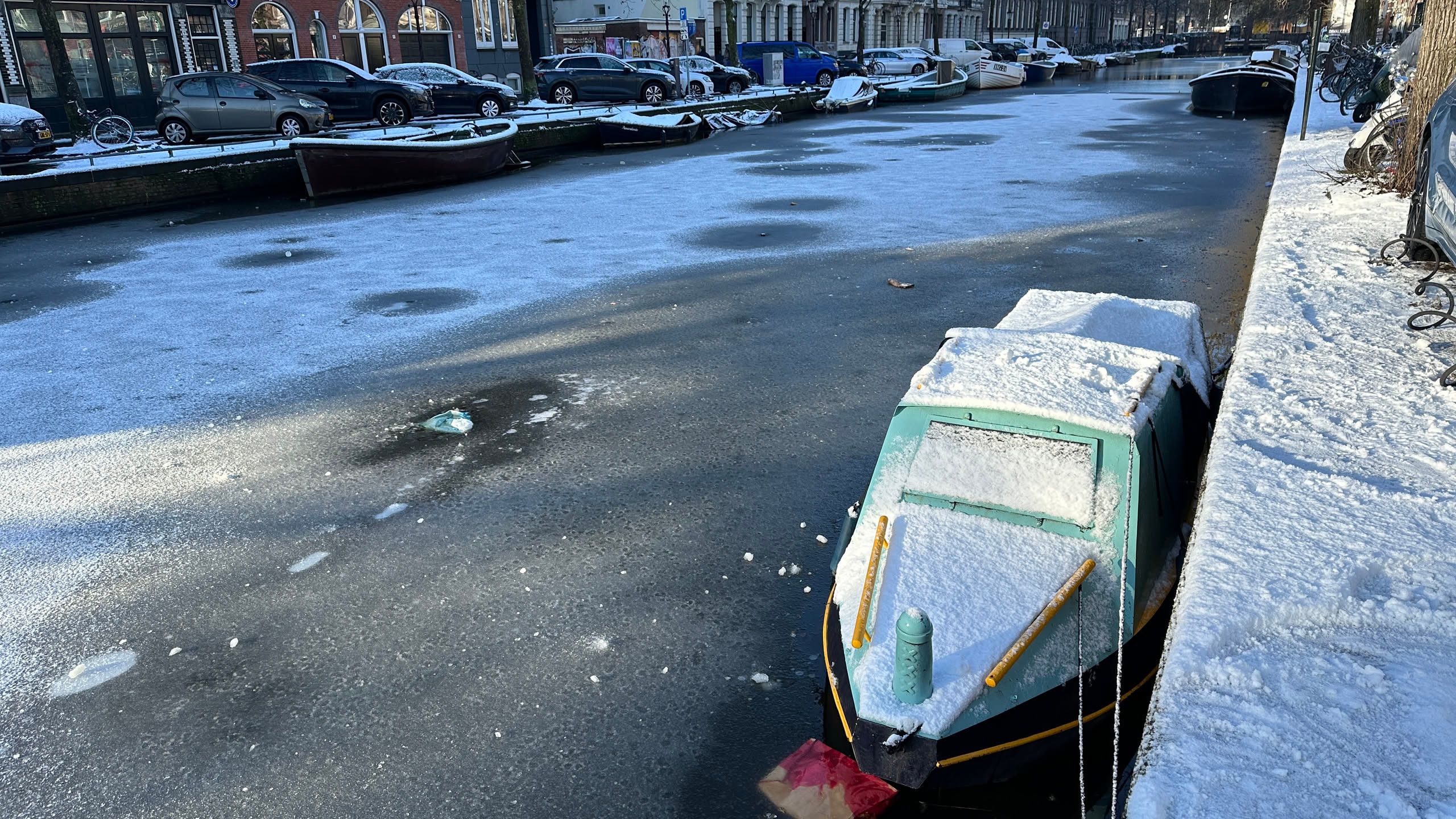 Canal with a very thin layer of ice and small boats covered in snow