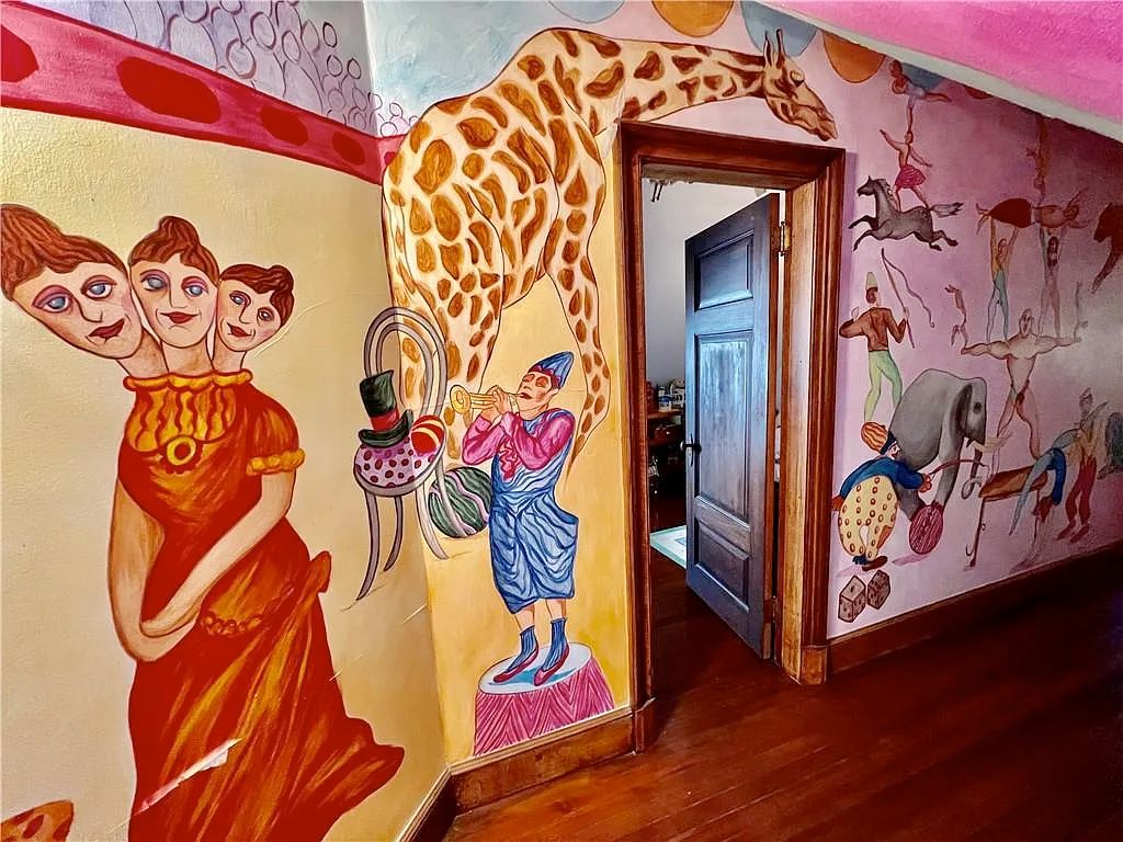 A crudely painted large mural with a woman with 3 heads, a huge giraffe, a clown, and other small circus related figures such as an elephant and a strong man. 
