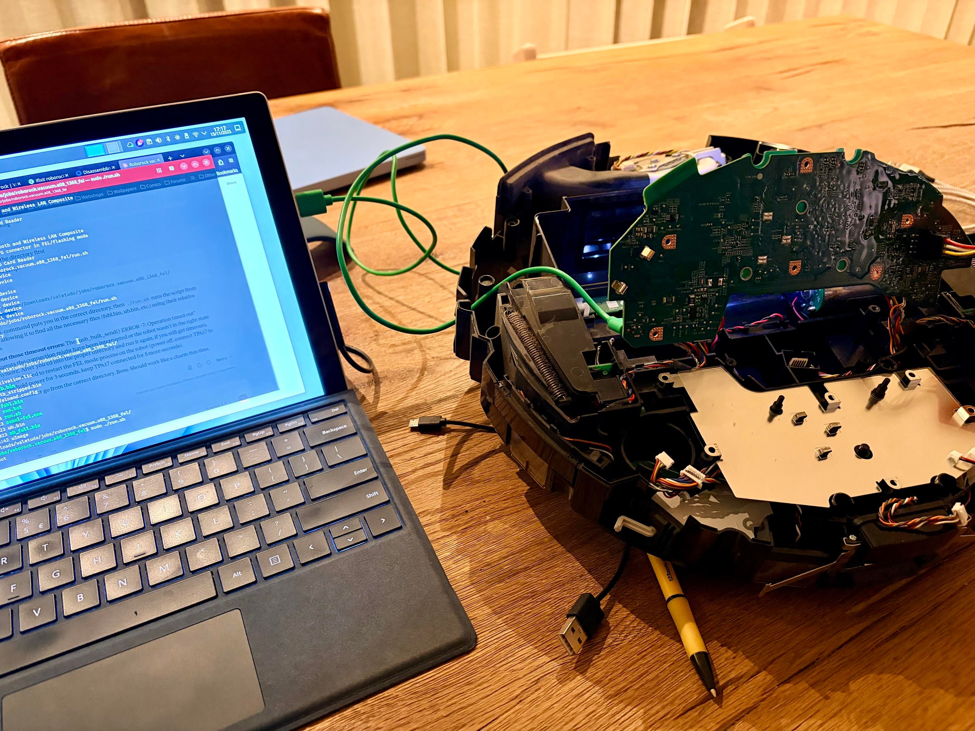 On the left is a Surface Pro running Bazzite. An open terminal ready to flash Valetudo firmware to the, via usb, connected Roborock S5 Pure. The S5 Pure is take apart. The main board is tilted and its connected to the battery and the laptop. Everything is set up on a wooden table. 