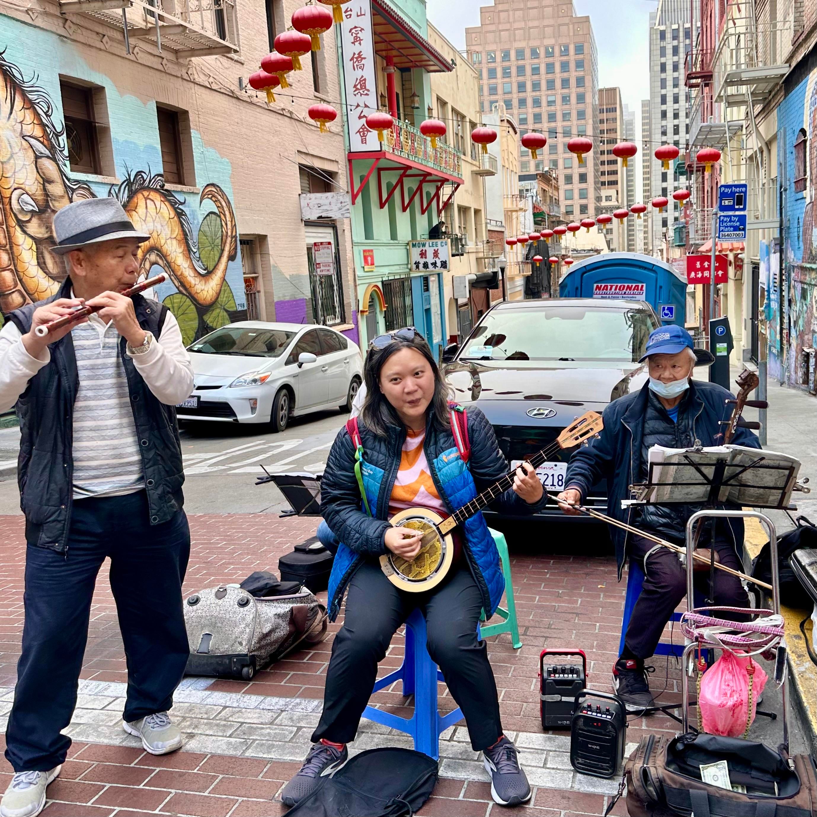 A photo of me sitting with a 3 piece band comprising old Chinese men playing traditional instruments in Chinatown 