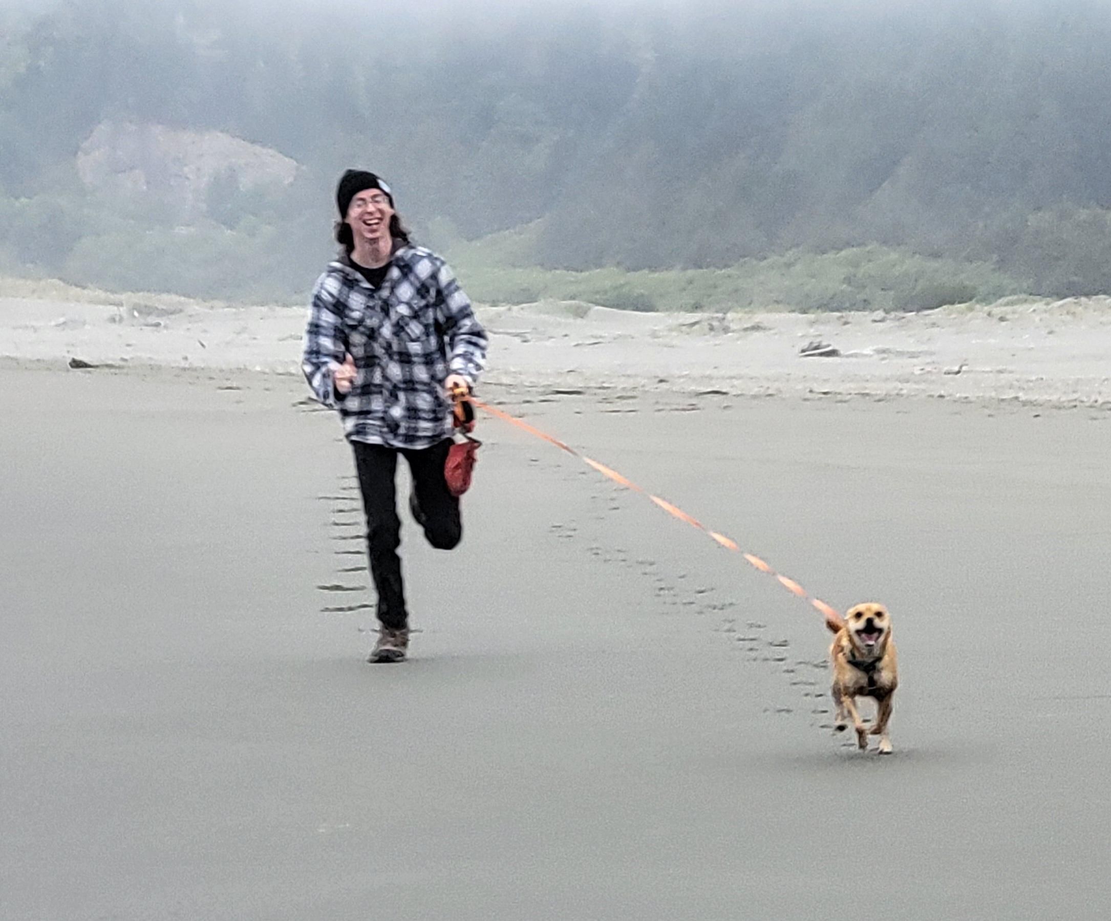 Happy cinnamon dog running on the foggy beach with her boy!