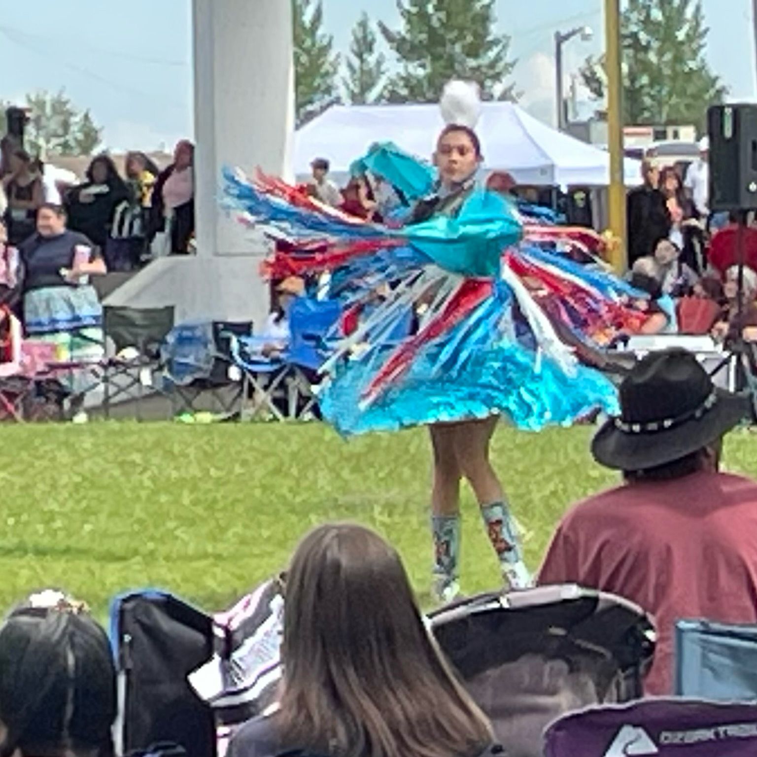 A fancy dancer in a turquoise dress and shawl with red, white, and blue fringes spins