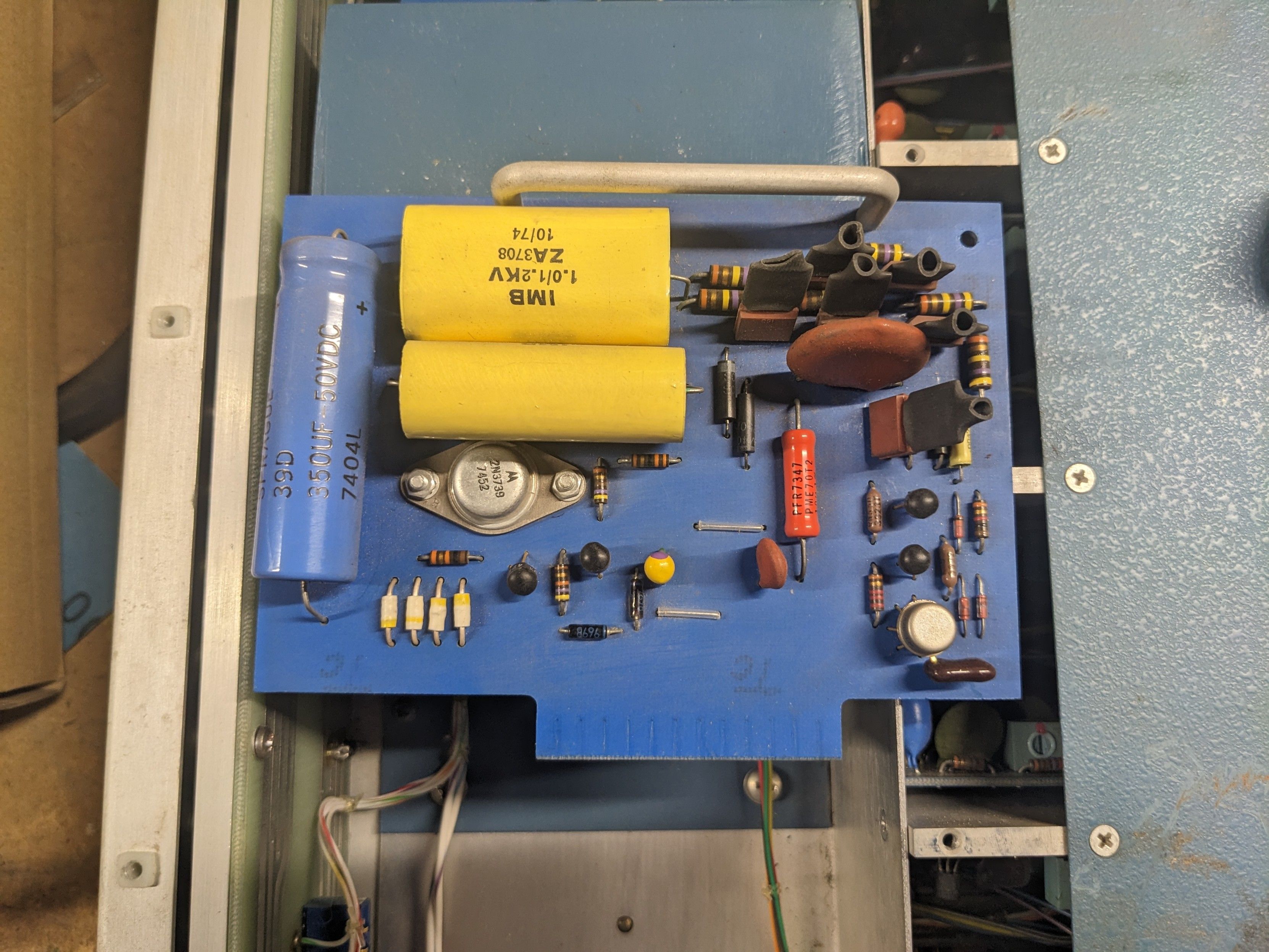 A pcb with matte blue solder mask.  It has 3 large capacitors and a thick, aluminum bar/handle.
