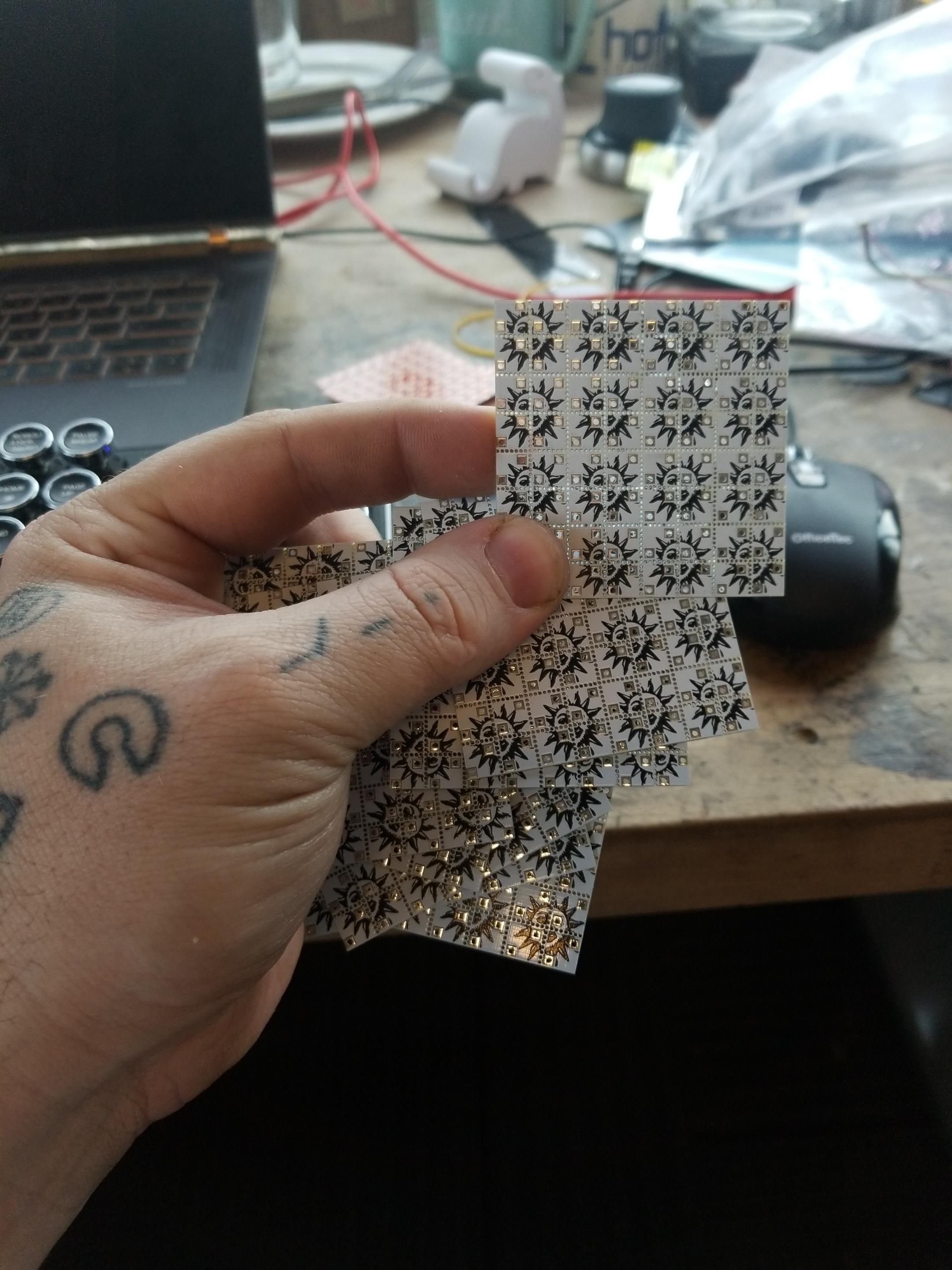 Small, thin, white PCBs with black psychedelic suns printed on them. They're divided into 1/4" square panels by mousebites. 