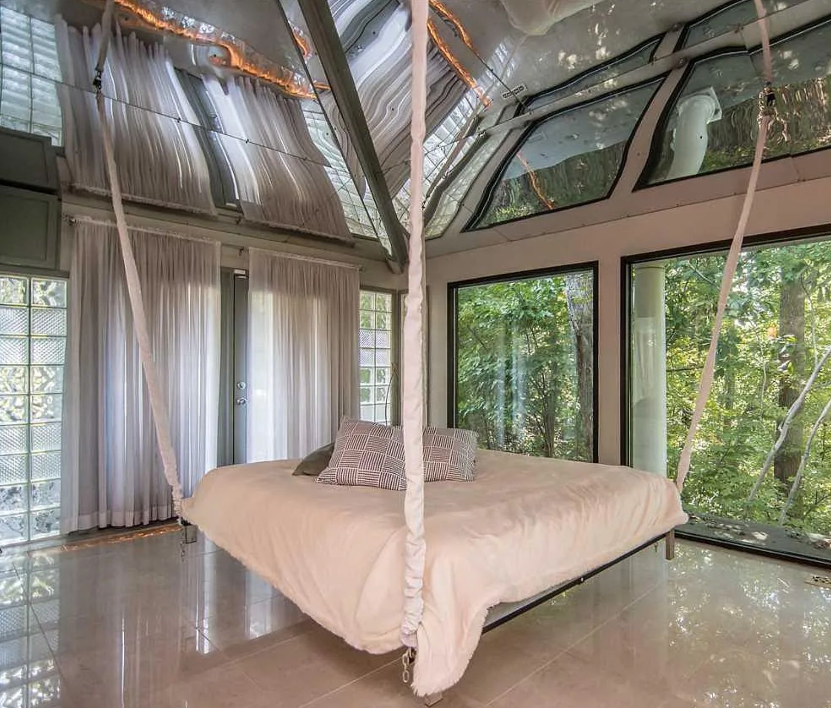 A bed that, for some reason, has ropes attached to the ceiling from all 4 corners of the bed, and there is a mirror above the bed as well. The bed actually has 4 legs underneath, but at first looks like it's hanging. 