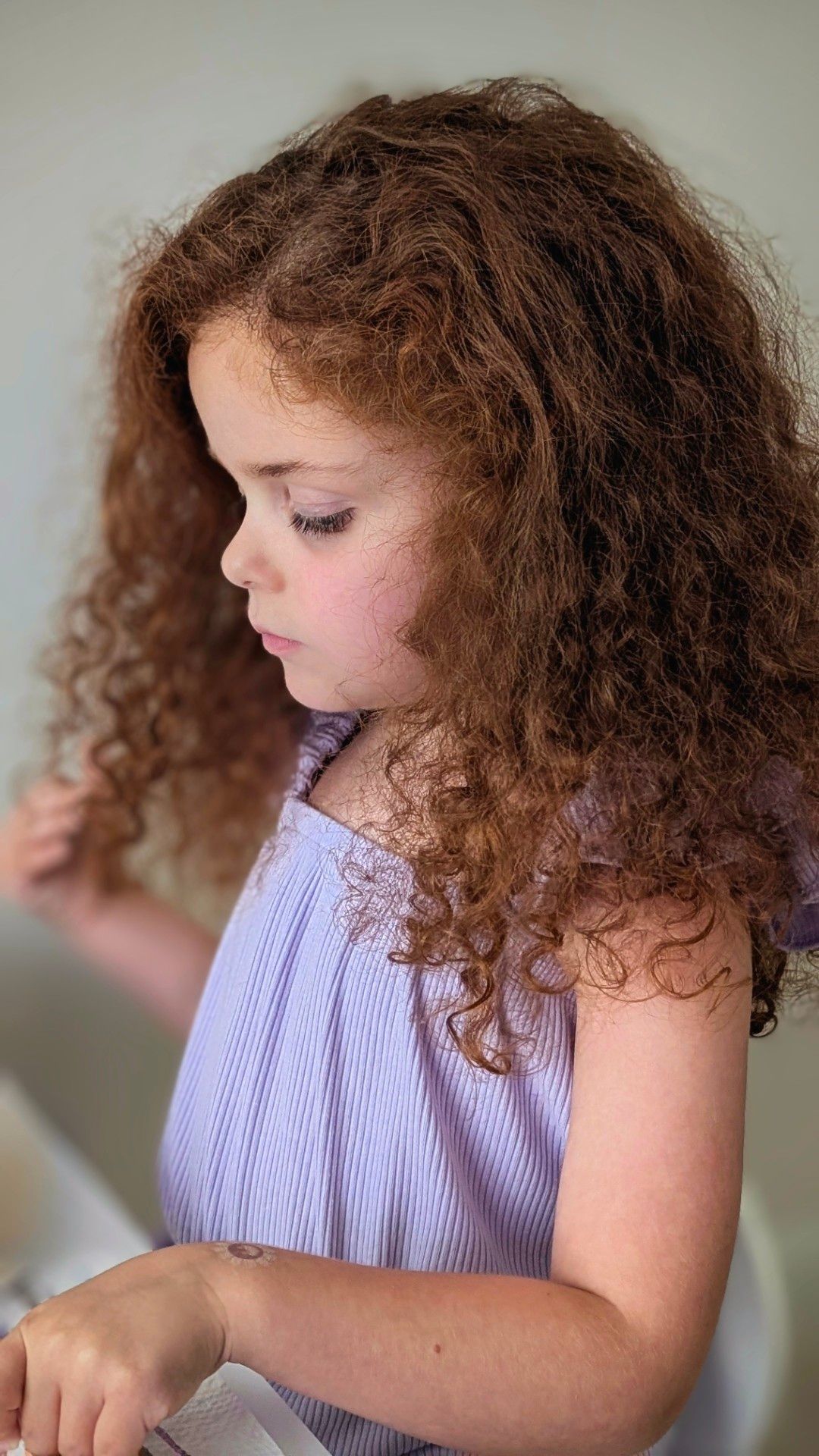 Portrait photo of little girl in profile with auburn hair so curly and unruly that its very existence makes the world a better place.