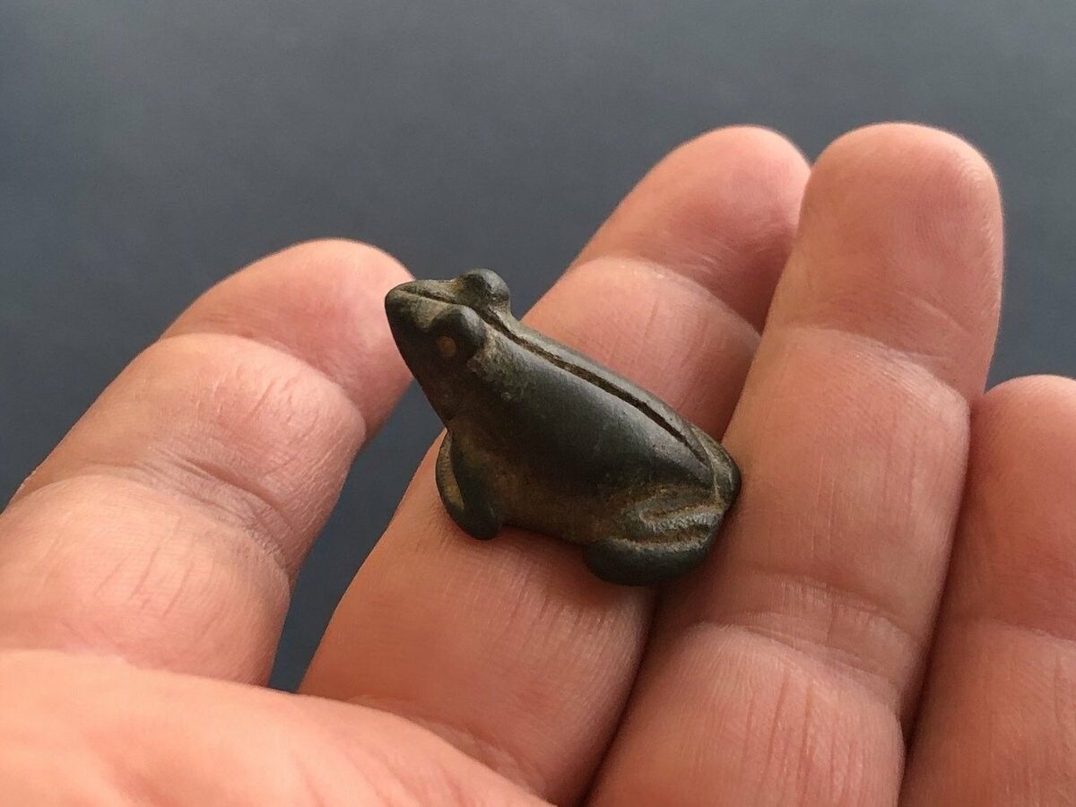 a hand holding a small carved stone frog