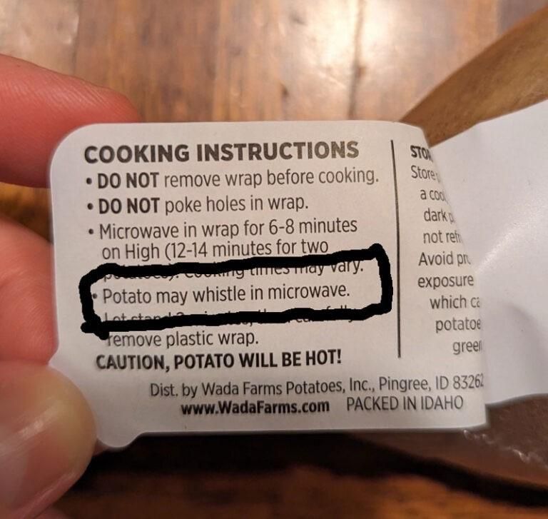 A hand is holding a cooking instruction label for a wrapped potato. Key points include warnings not to remove the wrap or poke holes, microwave cooking times, and a note that the potato may whistle in the microwave. The label advises caution, indicating the potato will be hot 