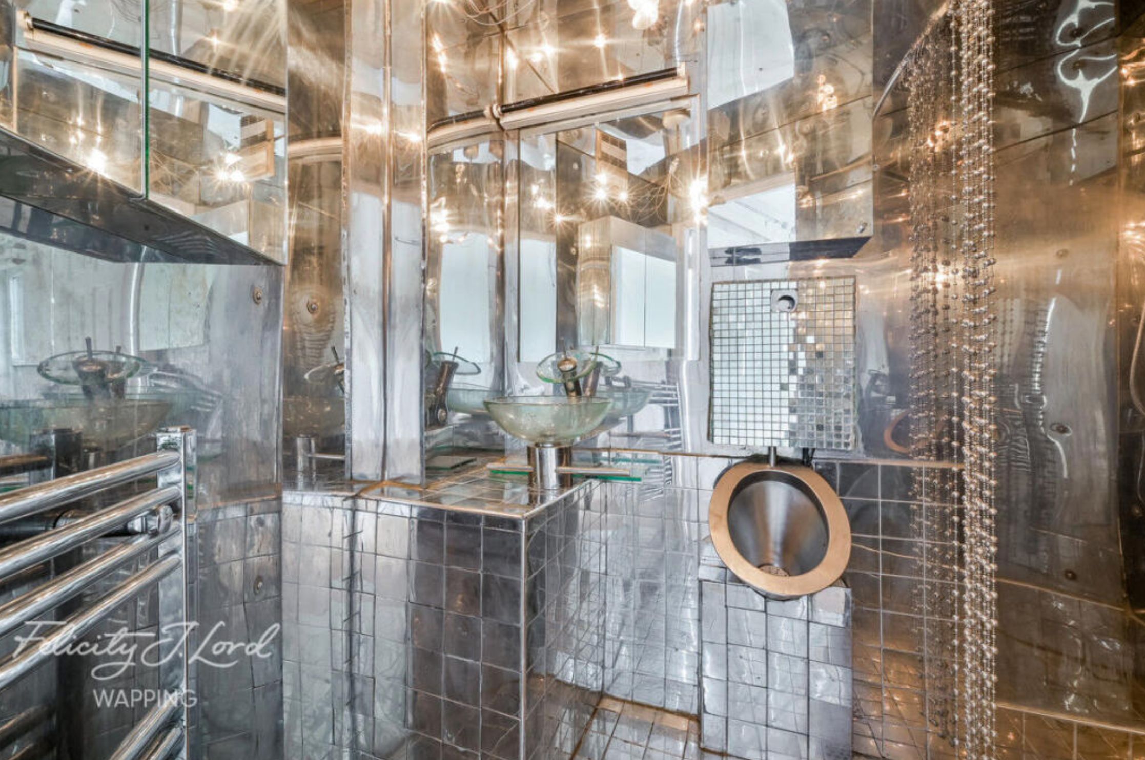 A bathroom where every surface is mirrored and it's extremely difficult to differentiate between the walls, ceiling, and the vanity and sink. 