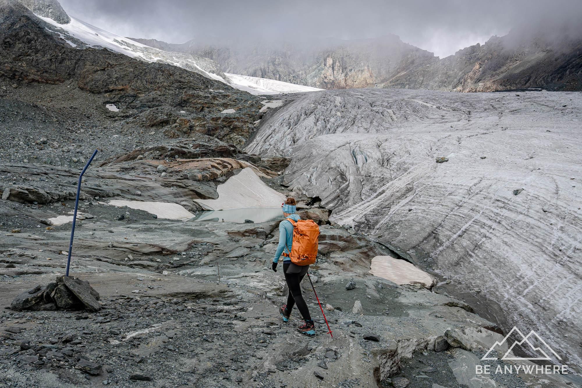 woman carrying a orange backpack hiking next to a glacier.