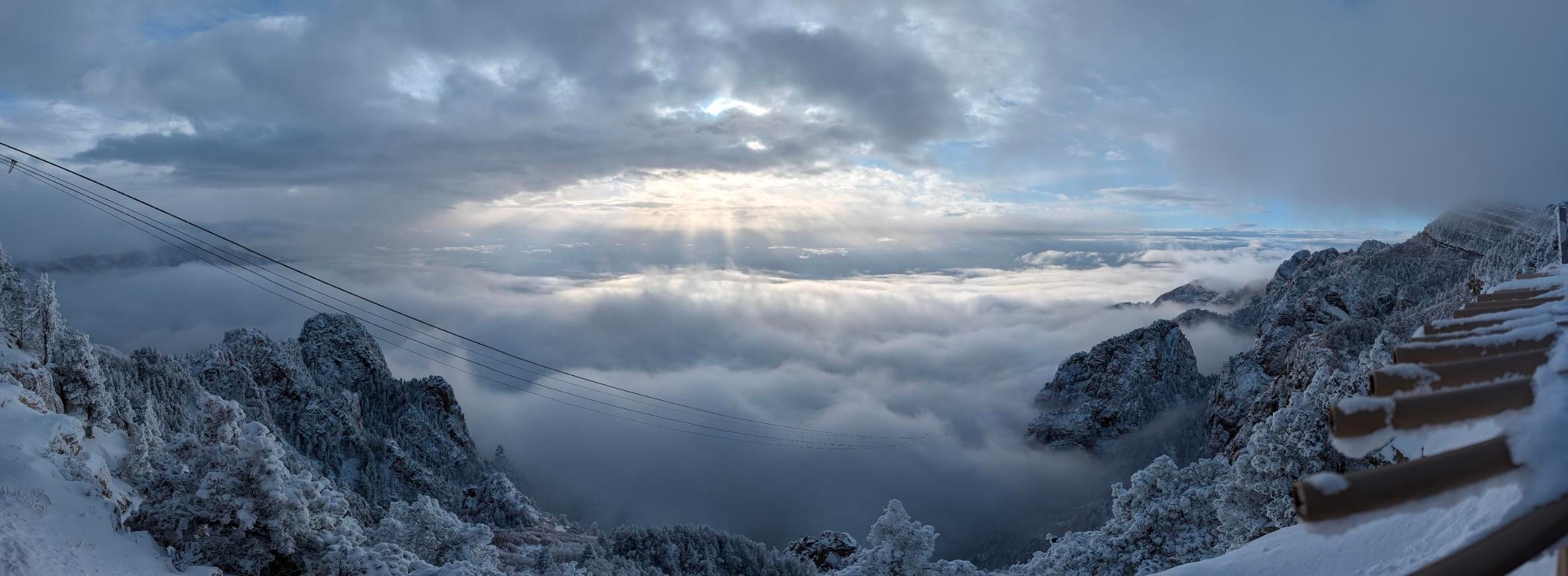 a view off a mountain with some cable car cables descending into a sea of clouds above and below, with snow-topped mountains poking through everywhere