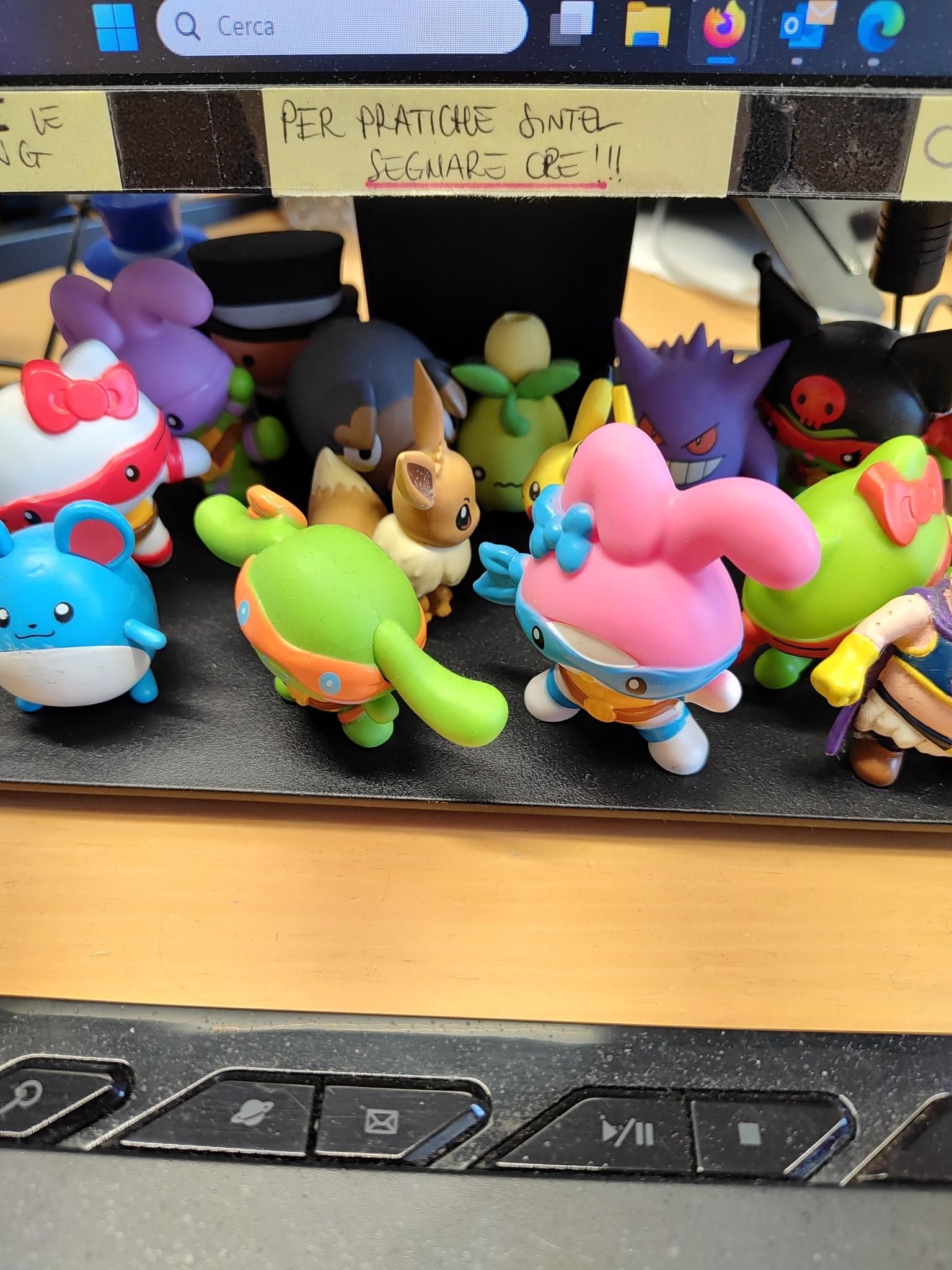 una base di un monitor affollata di pupazzetti (collab TMNTxSanrio del McDonaldo), varie gomme Pokemon e si intuisce un piccolo Majin Bu grassone a destra