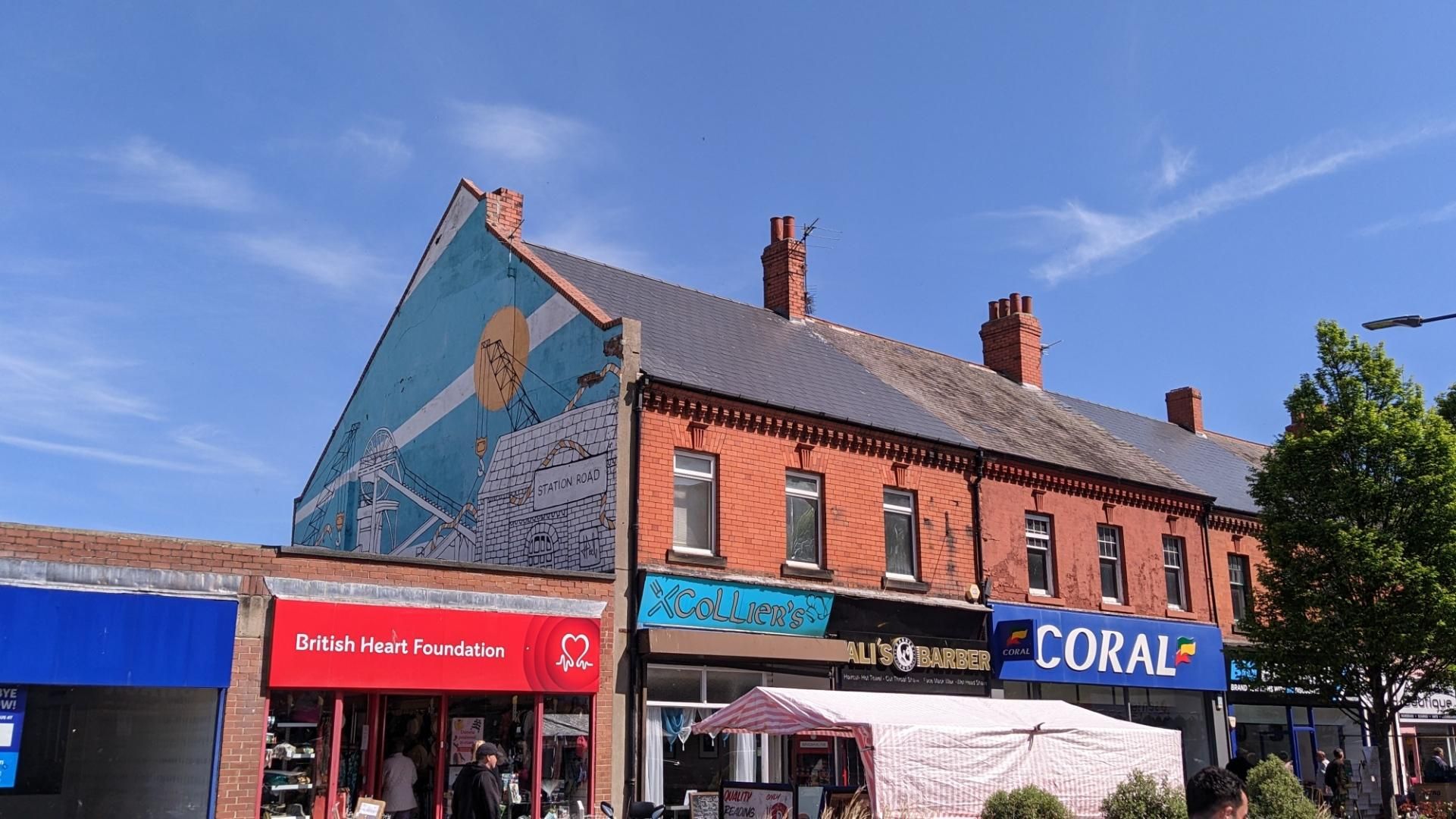 Station road: Brick buildings with shops and large graffiti showing coal mining