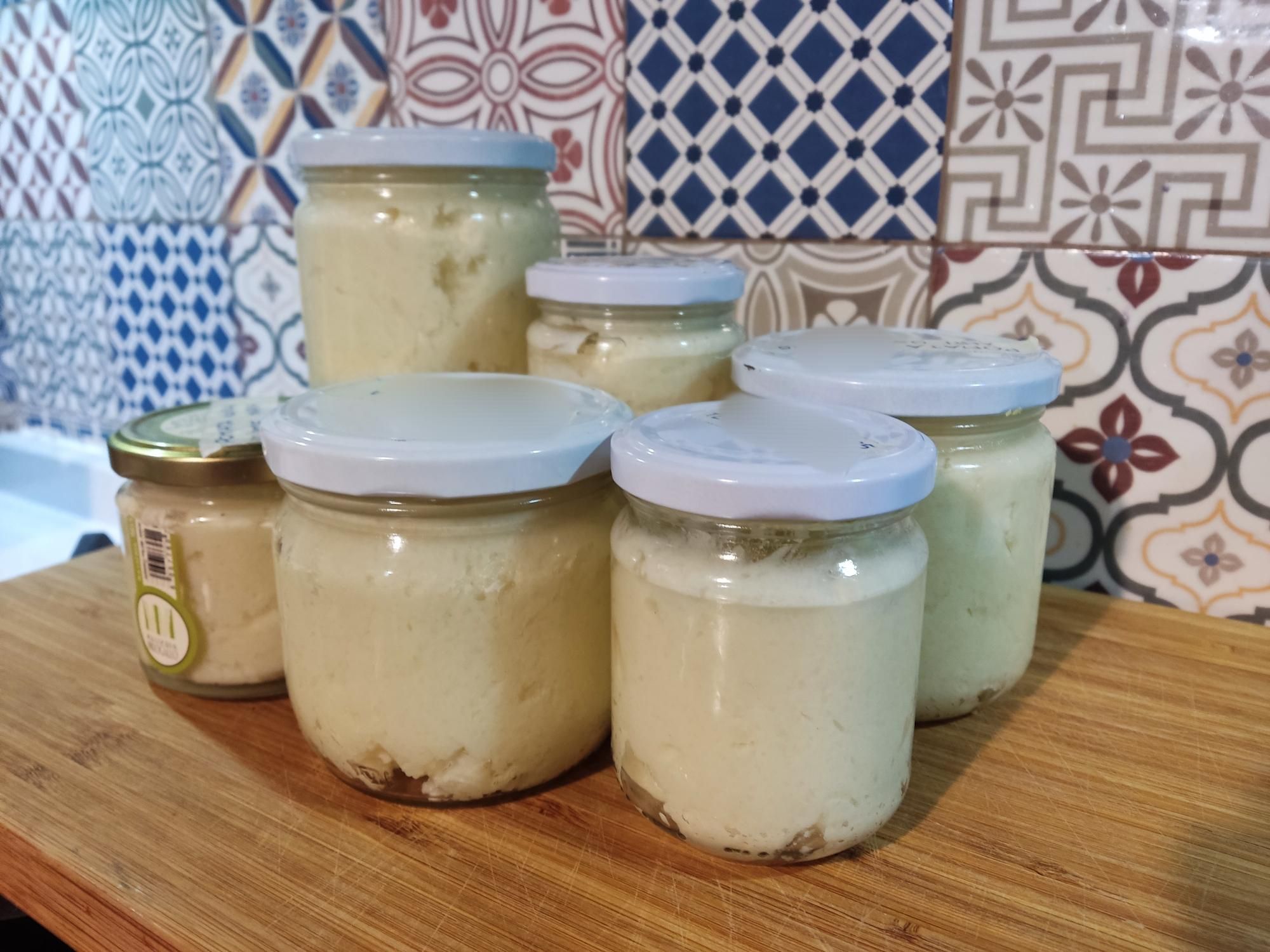 6 barattoli di diverse misure pieni di una pomata beoge, su un tagliere di legno e sullo sfondo mattonelle di diverse fantasie geometriche