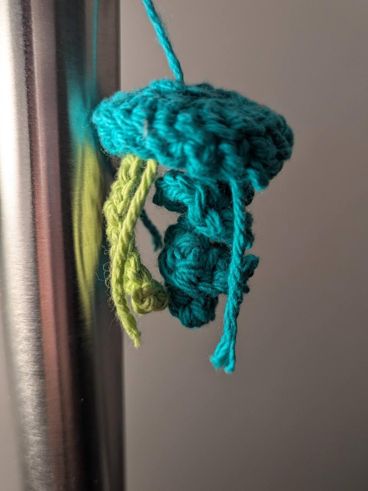 Small - about the size of a big thumb - jellyfish crochet in blue and a few strands if yellowish green yarn