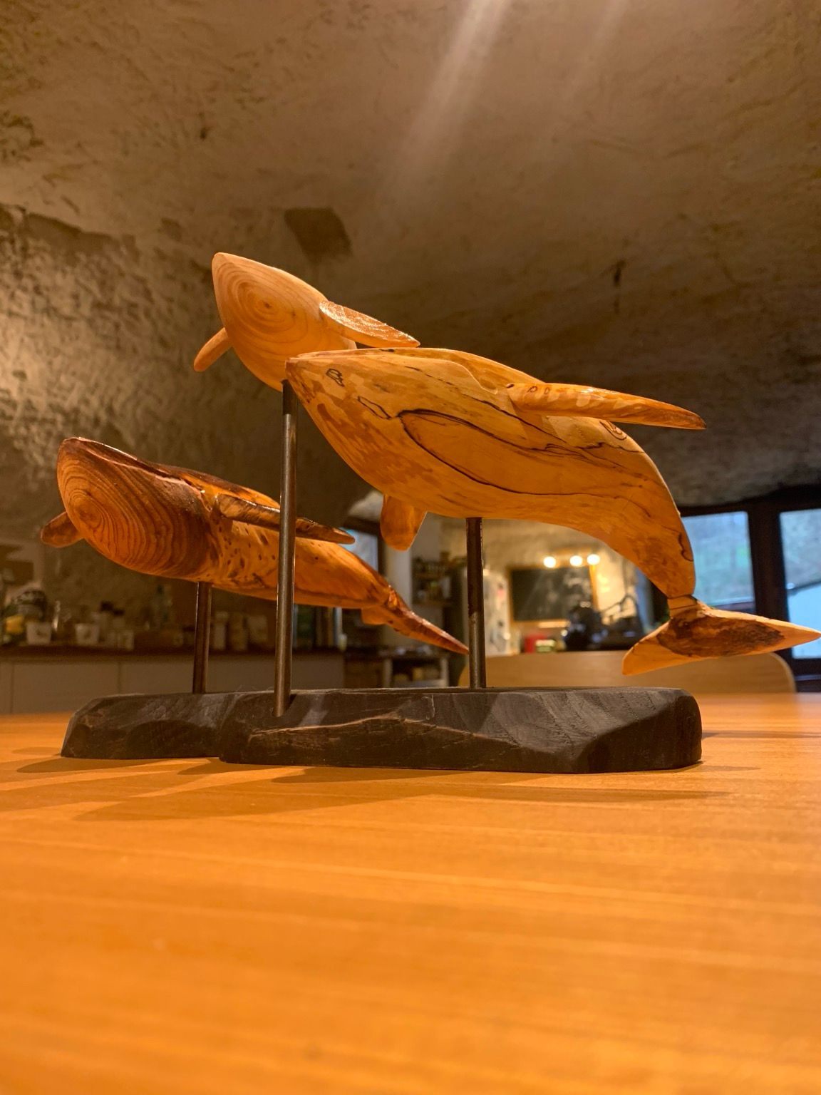 Sculptures de deux baleines en bois entourant un baleineau, montées sur un socle noir