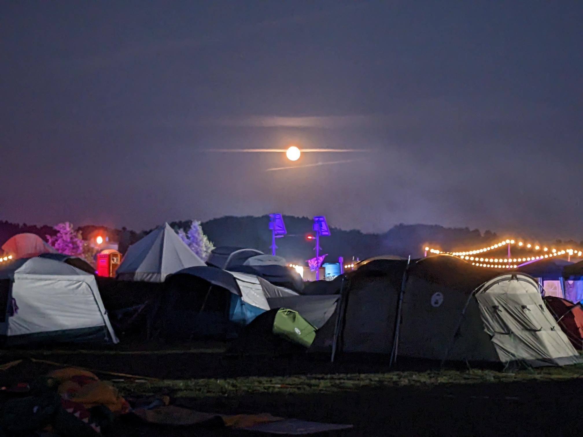 A photo of a full moon over tents and colorful lights.