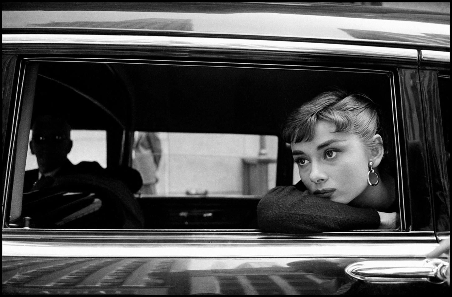 Audrey looks sadly out the back window of a limousine. 