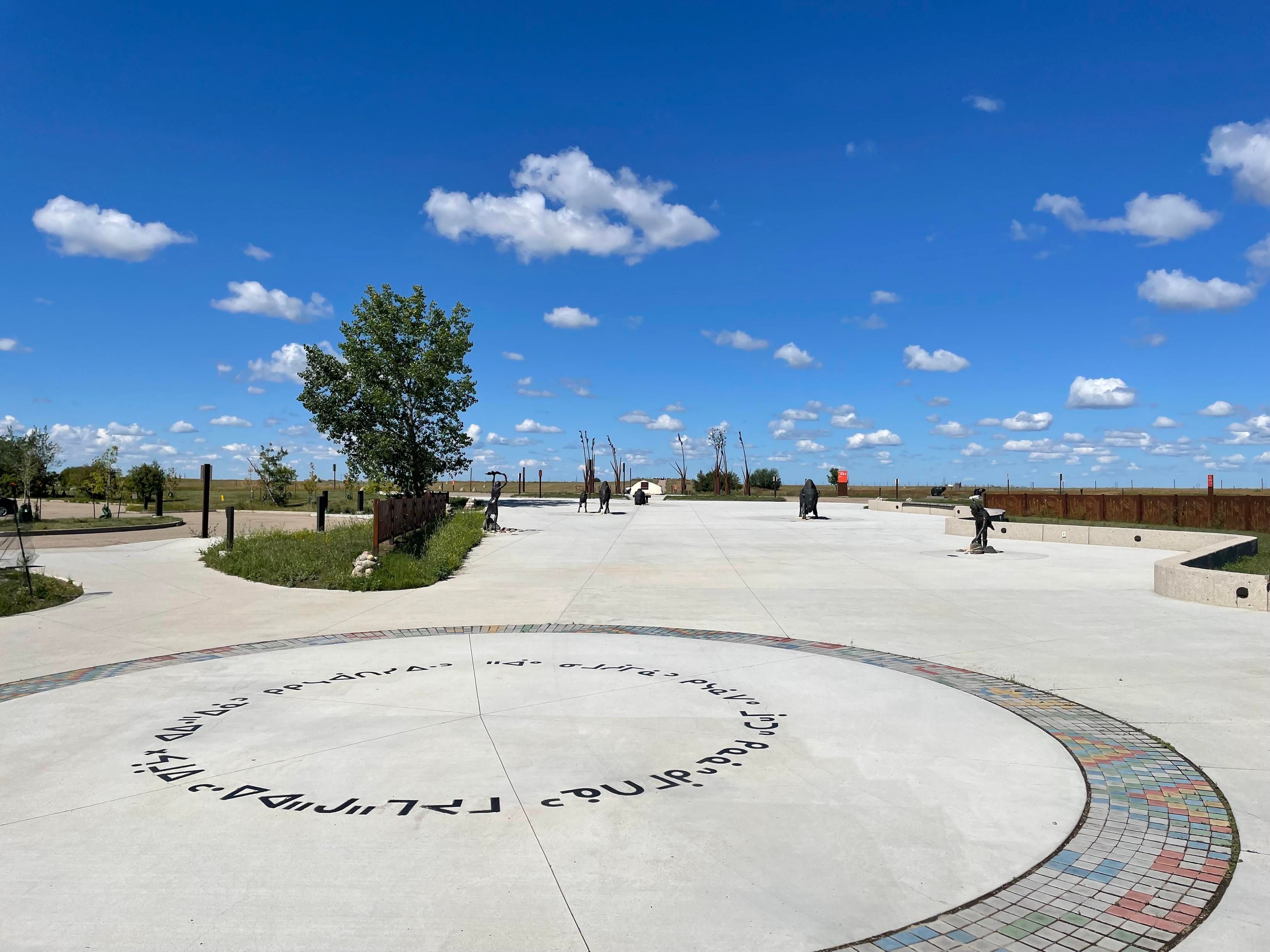 A large granite area with a paved indigenous circle under puffy cloud blue sky