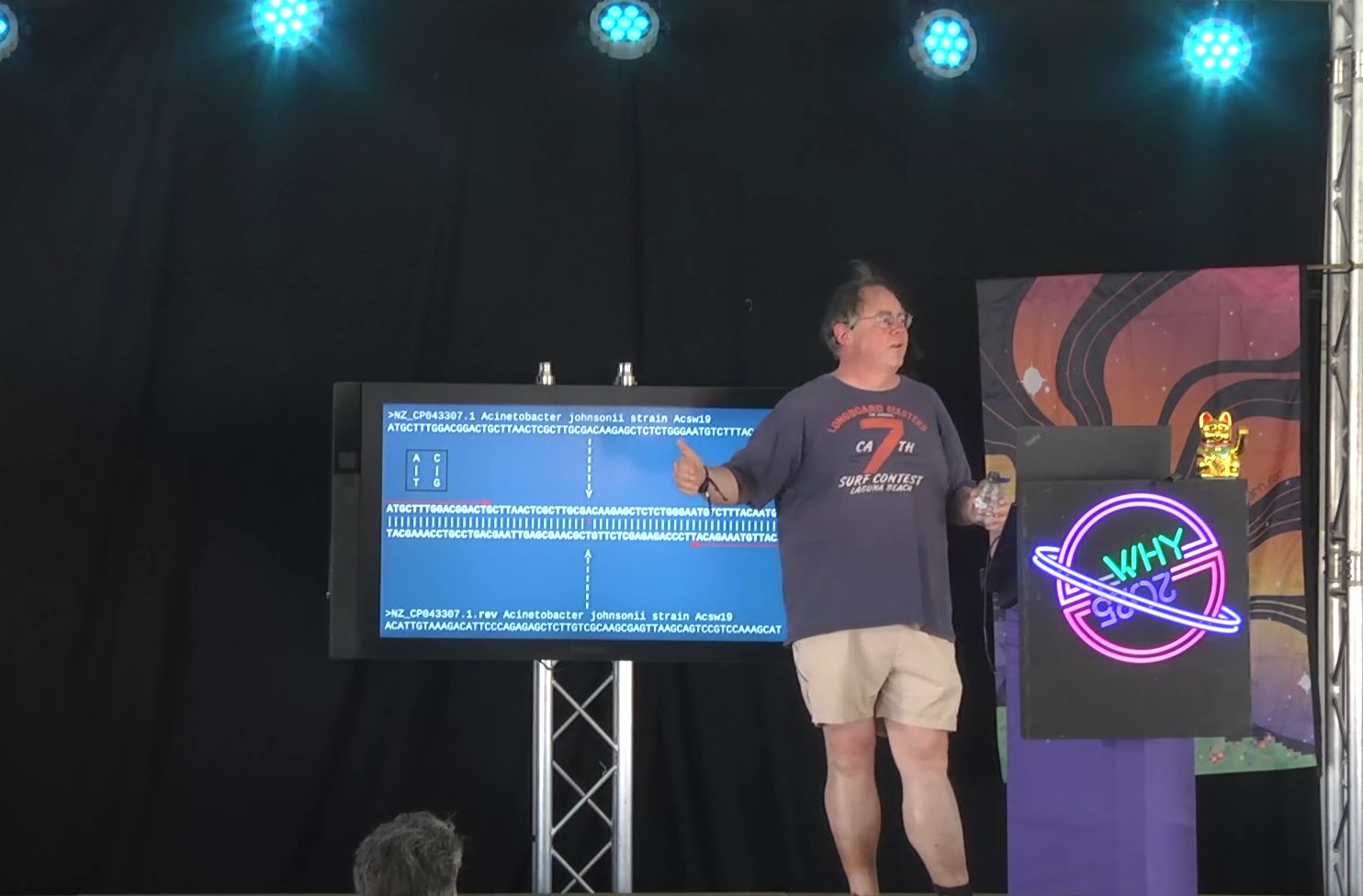 bert hubert on stage in front of a screen full of DNA. Bert is wearing shorts and a t-shirt. 