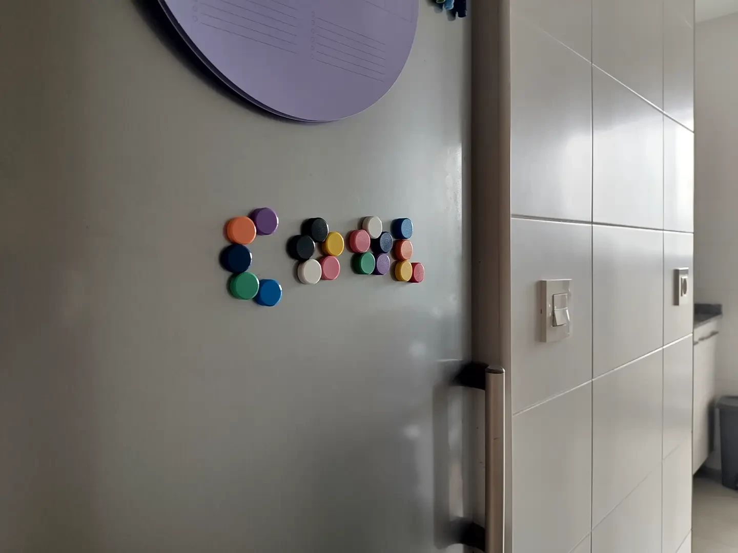 colorful round magnets on a grey fridge spelling the word "cool"