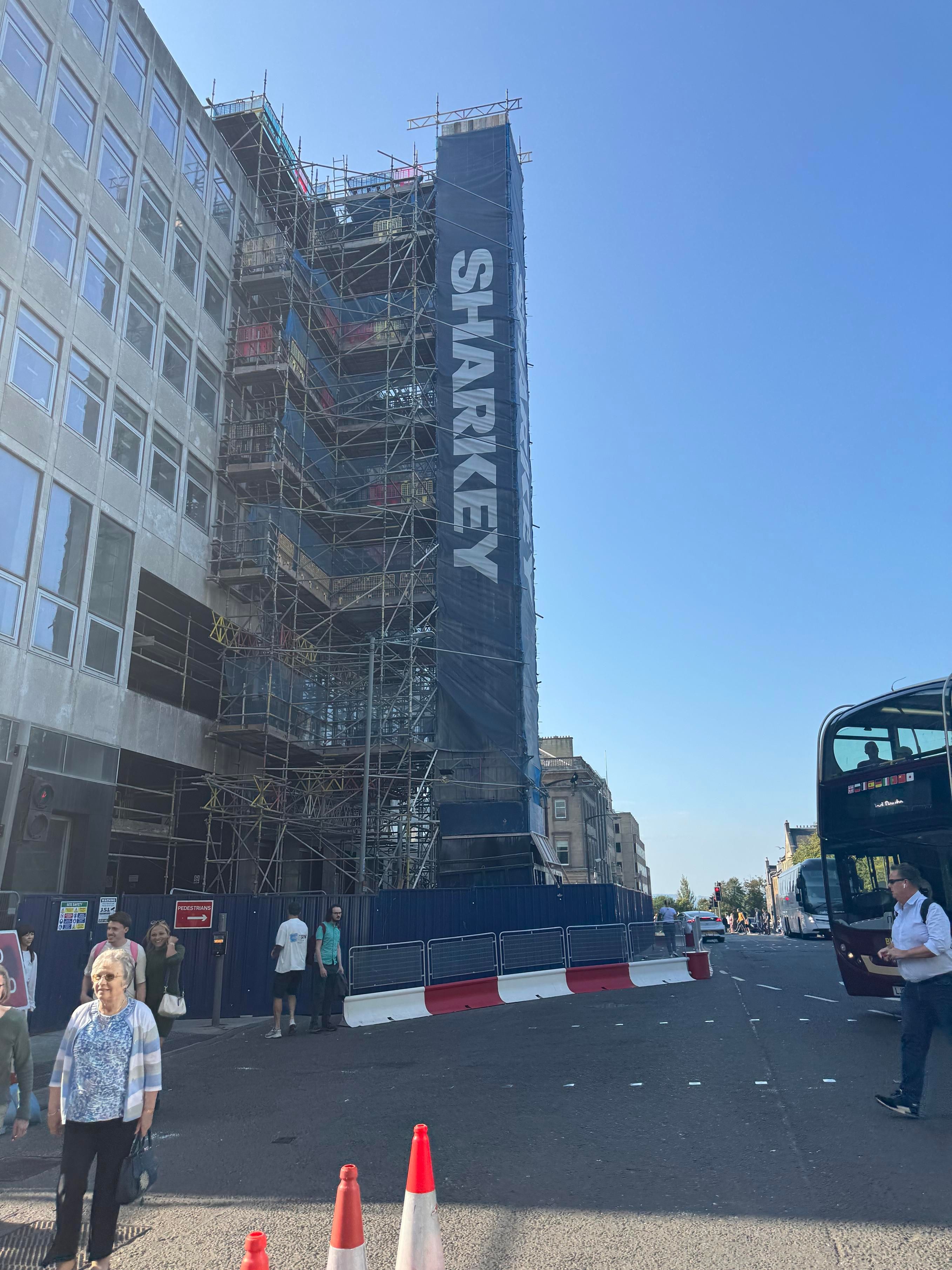 A building with scaffolding. The work Sharkey is printed on the scaffolding covers