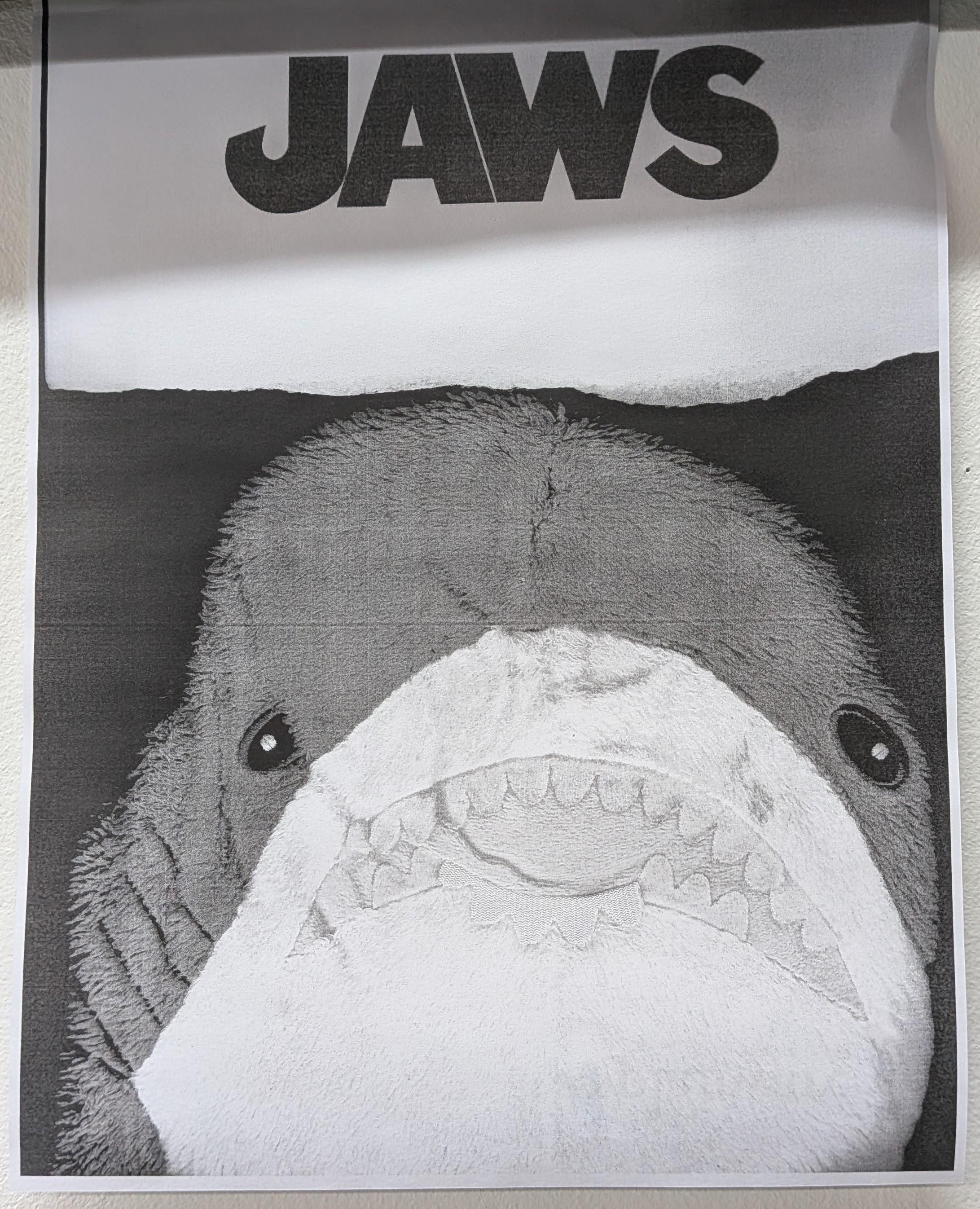 A b/w photocopy image of a small blahaj with the text "JAWS" above, printed on a piece of paper with a torn edge. The blahaj is squished against the glass of the copier. The composition is reminiscent of the movie poster.