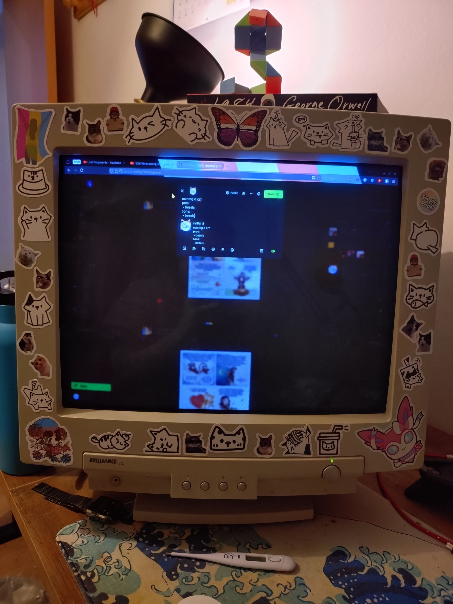 a frontal picture of a crt whose beige bezel is stickerbombed with little cats and a pride sticker on the upper left, lower left and bottom right corners