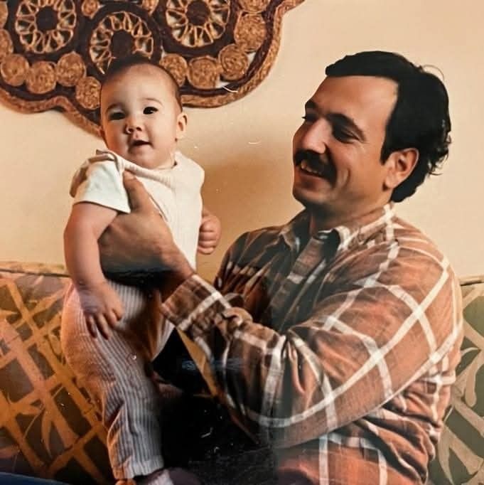 Latino looking man in brown flannel shirt holding a baby.