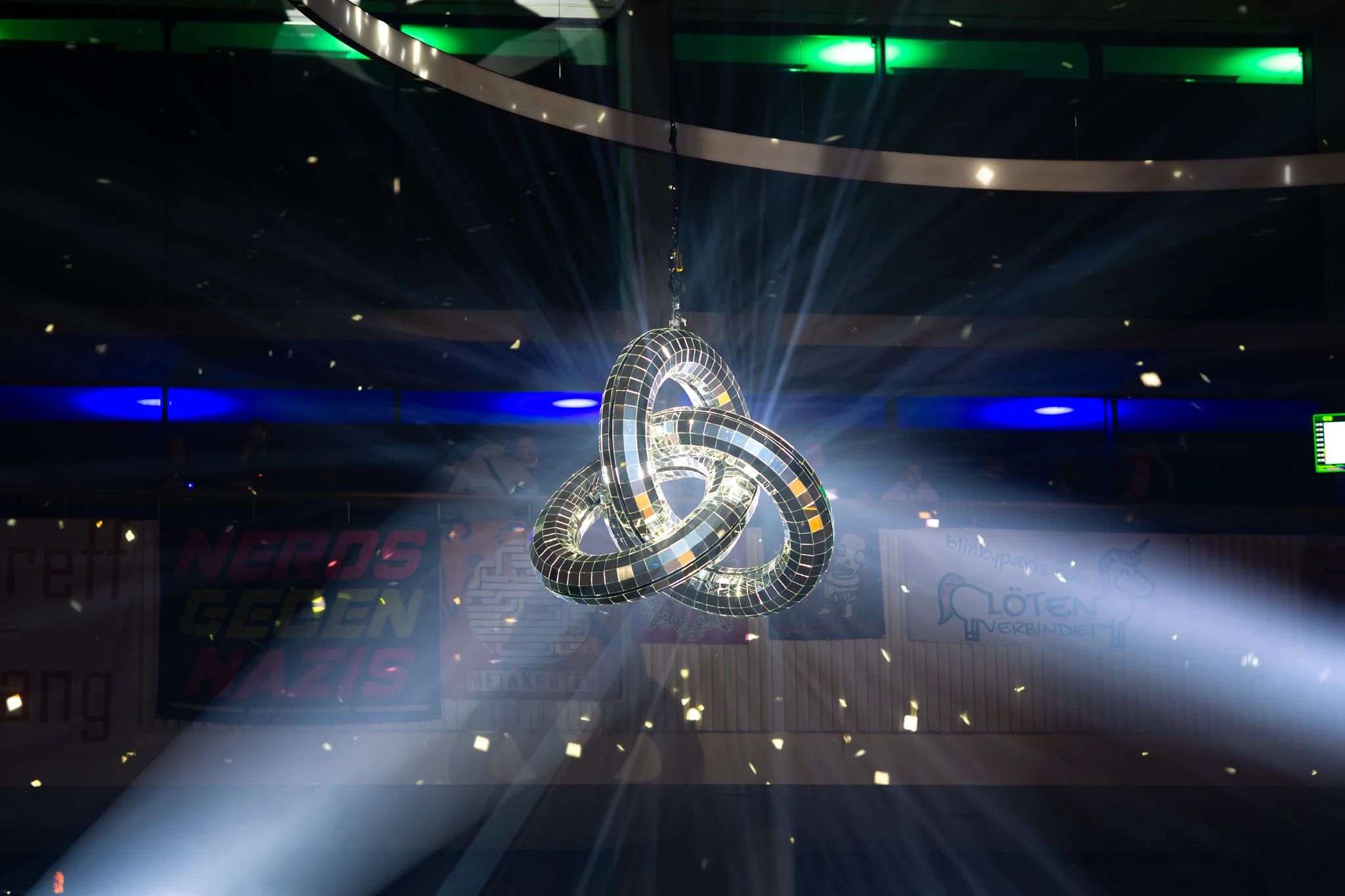 the same structure as in the other image from a different angle and with two spotlights. in the background, some posters are hanging off a balcony; the windows to different parts of the building in the background are lit up in blue and green.